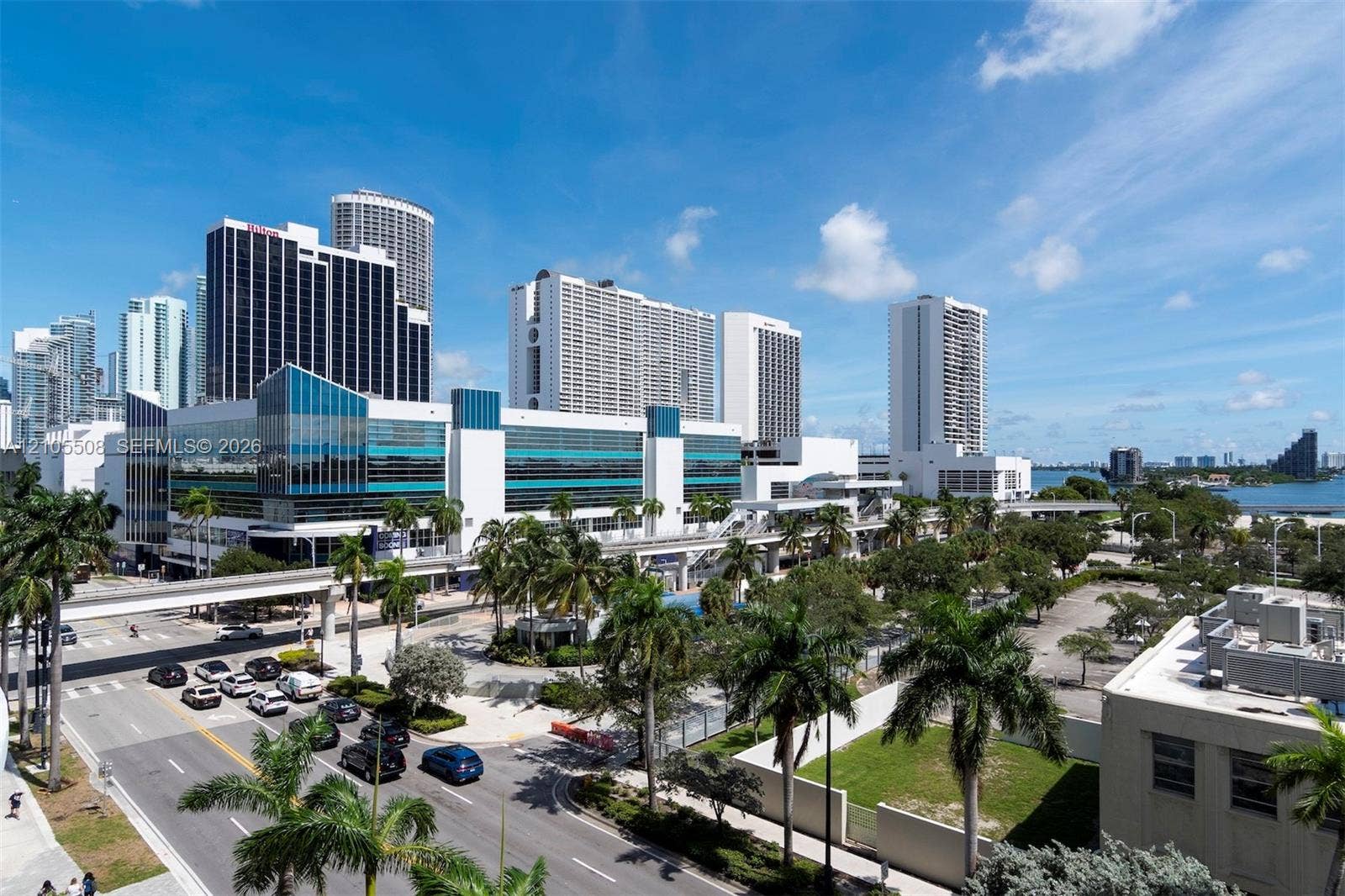 Urban skyline with multiple high-rise structures, extensive palm tree landscaping, and a broad waterway in the background