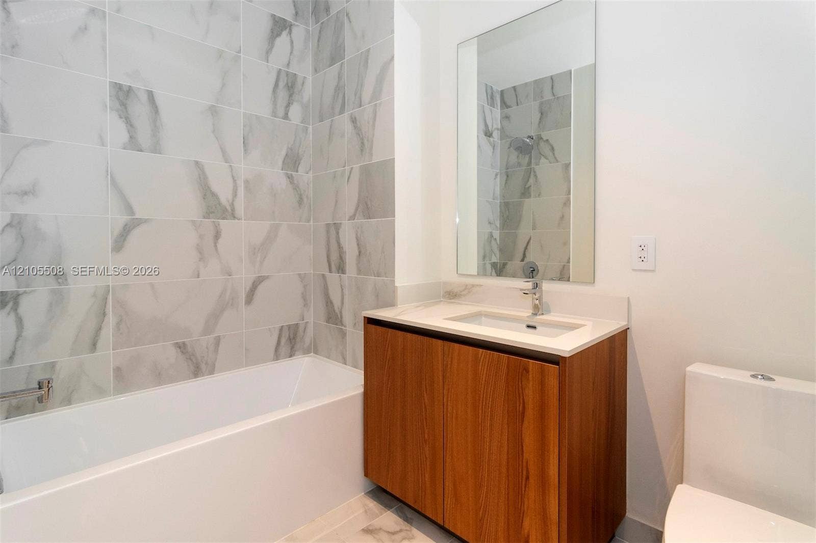 Bathtub with subway tile surround, wood-finish vanity with countertop, and rectangular wall-mounted mirror