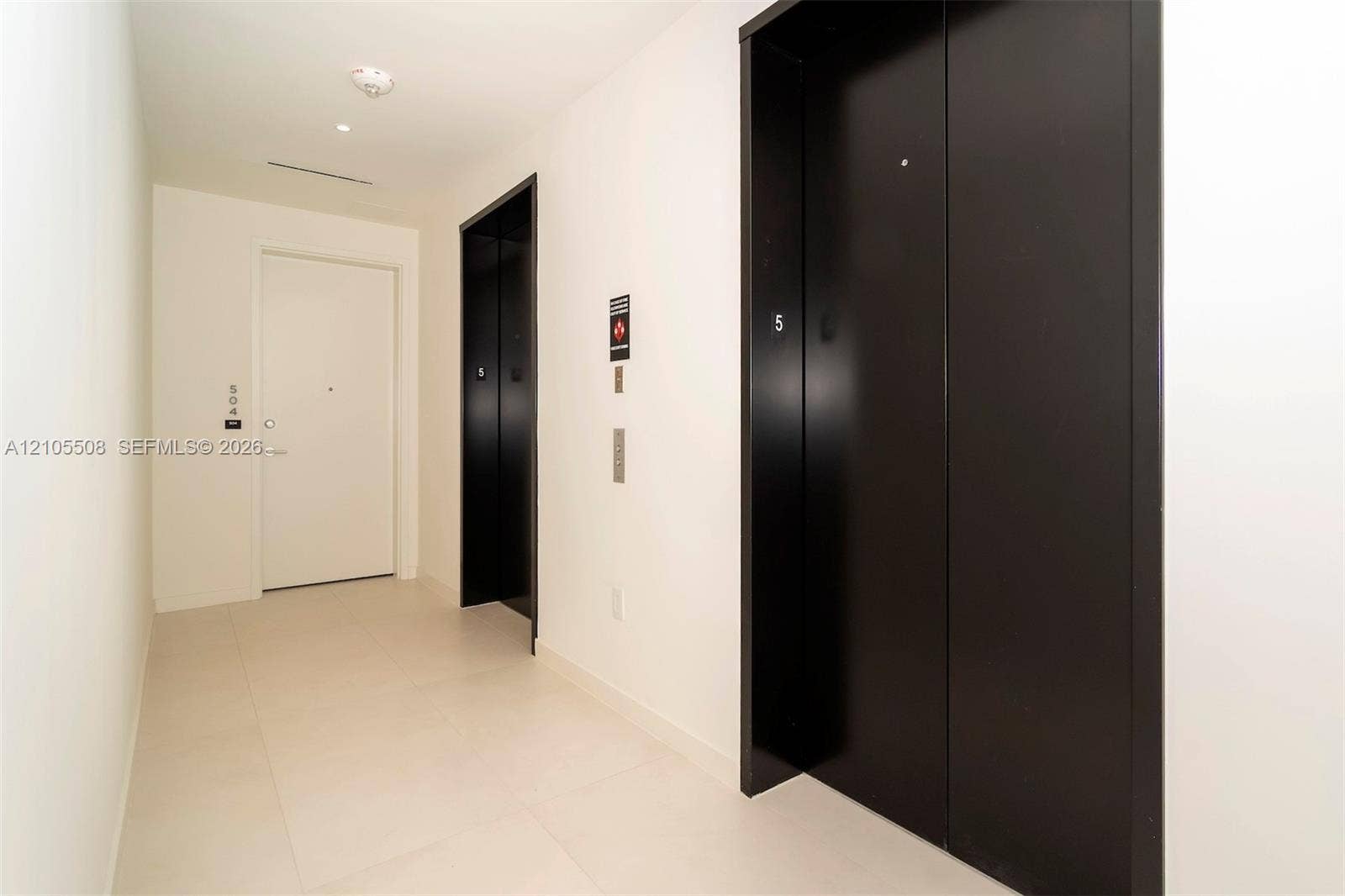 Light-toned tile flooring, white walls, and two dark-paneled elevators