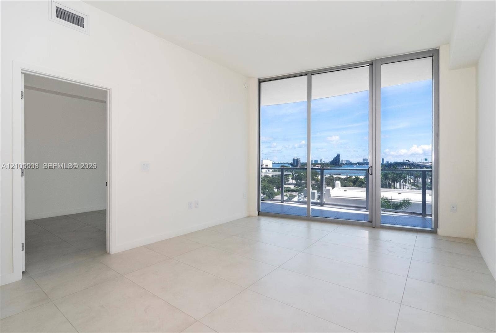 Sliding glass doors opening to a balcony with metal railings, tile flooring, and white walls