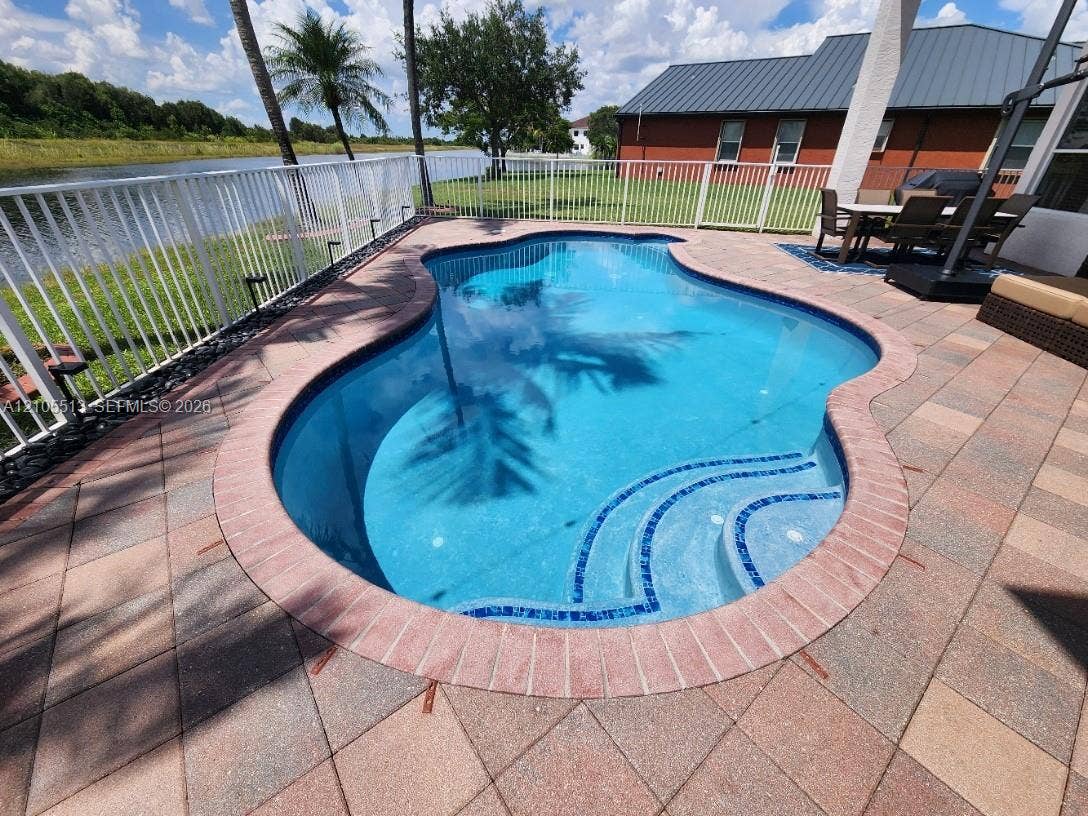 Newly resurfaced saltwater freeform swimming pool with auto cleaning system, integrated steps, brick coping, and a paver patio