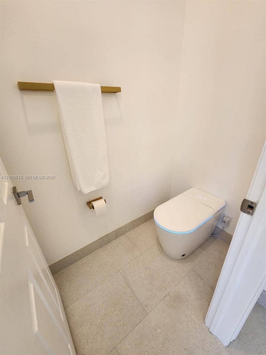 White walls with a modern smart toilet, porcelain flooring, and matching gold-finish fixtures