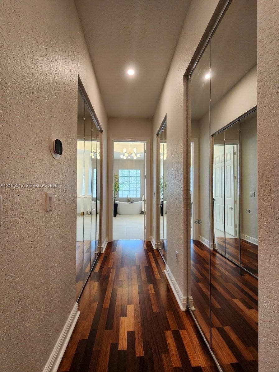 Hallway featuring hardwood flooring, mirrored closet doors, recessed lighting, and white baseboards