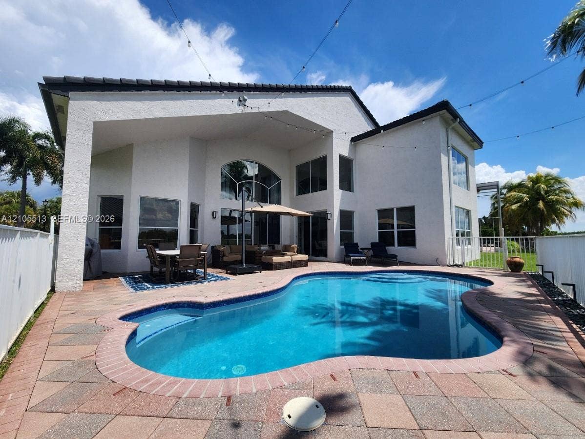Custom-shaped swimming pool with integrated steps, paver decking, and a covered patio