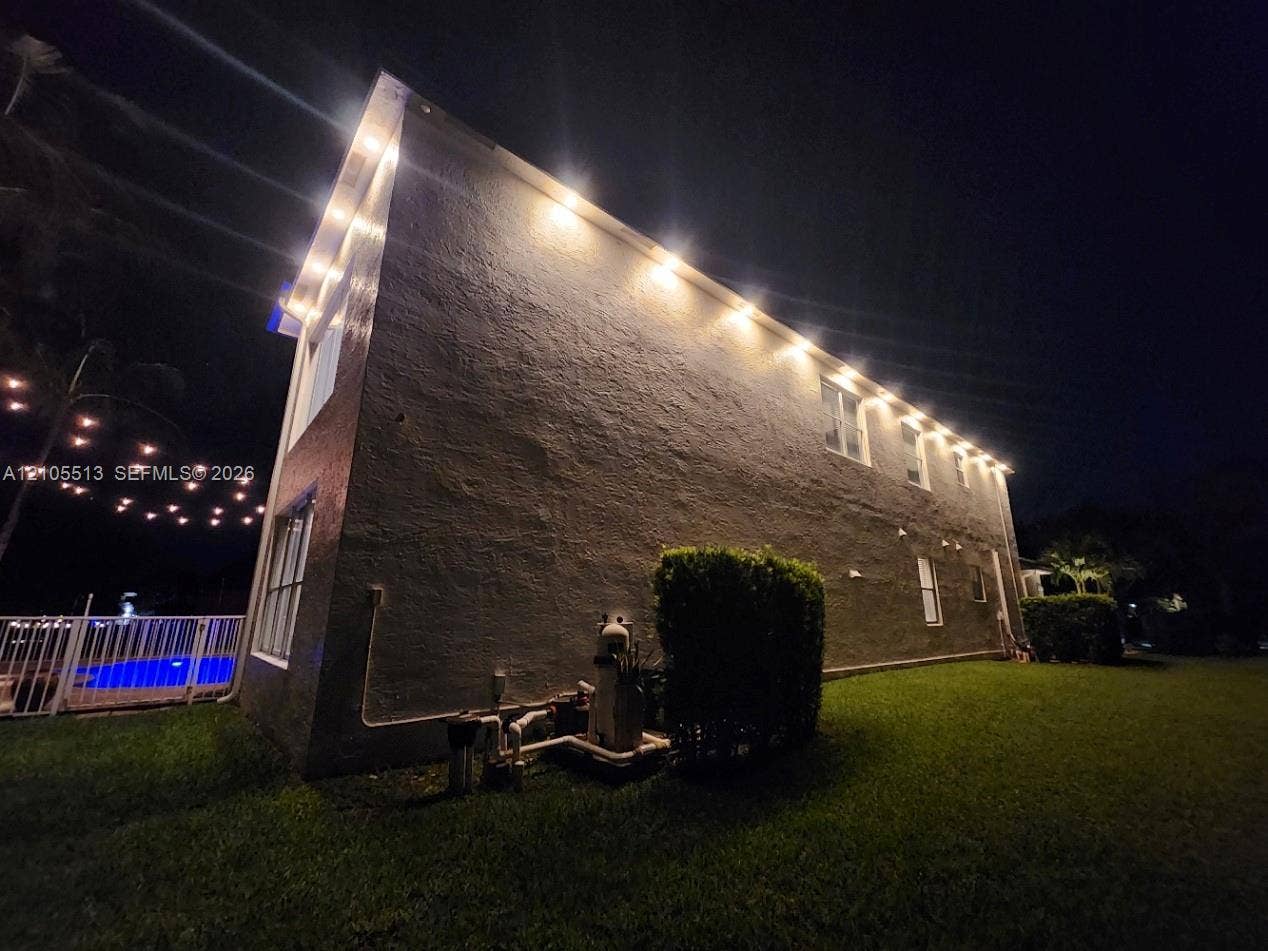 Night view of side with automated security down lighting, low voltage string lights & multi-colored pool light