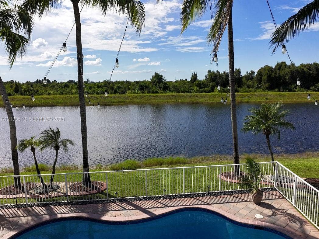 Freeform swimming pool with paver decking, white perimeter fencing, and mature palm trees