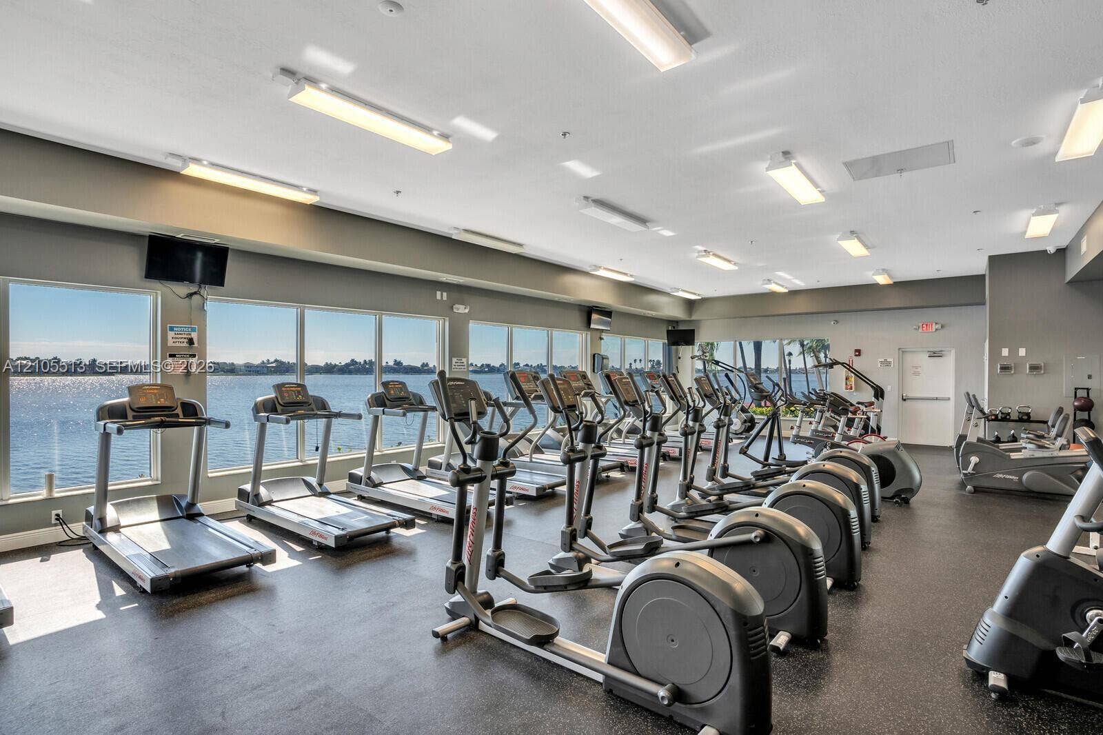 Fitness center featuring full-length floor-to-ceiling windows, water frontage, rubberized flooring, and recessed linear lighting