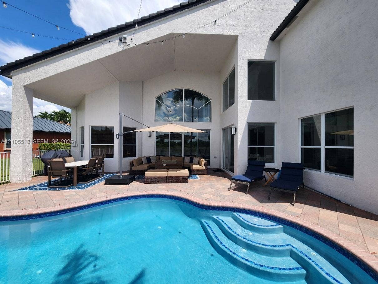 Outdoor living area featuring a swimming pool with integrated steps, a covered patio, and room for a deep seating set, dining set & lounge chairs