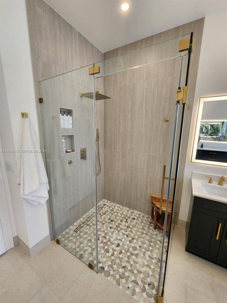 Glass-enclosed shower with custom marble tiled flooring, a built-in shower niche, and a rain shower head