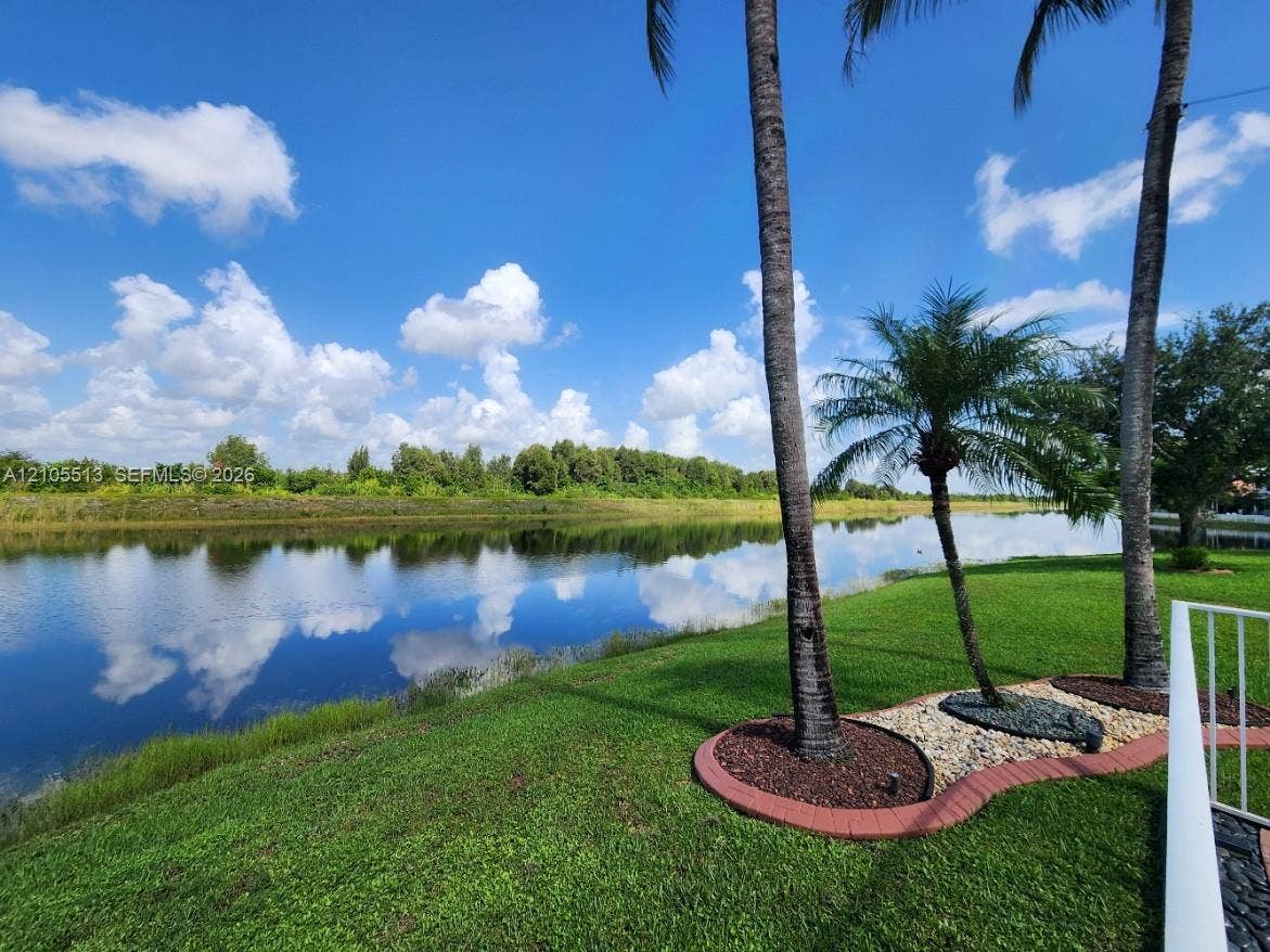 Lakeside property featuring a manicured lawn, established palm trees, and decorative rock landscaping