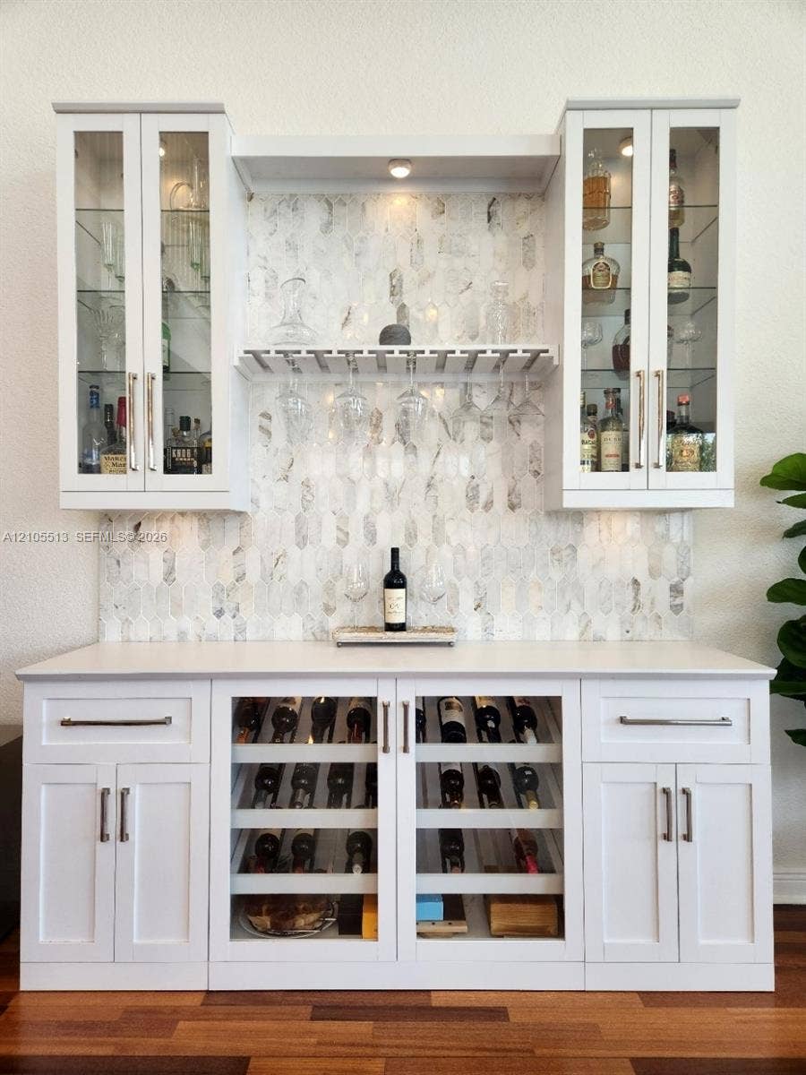 Custom built-in bar featuring upper glass-front cabinetry, a marble backsplash, under-cabinet lighting, and integrated wine storage with glass doors