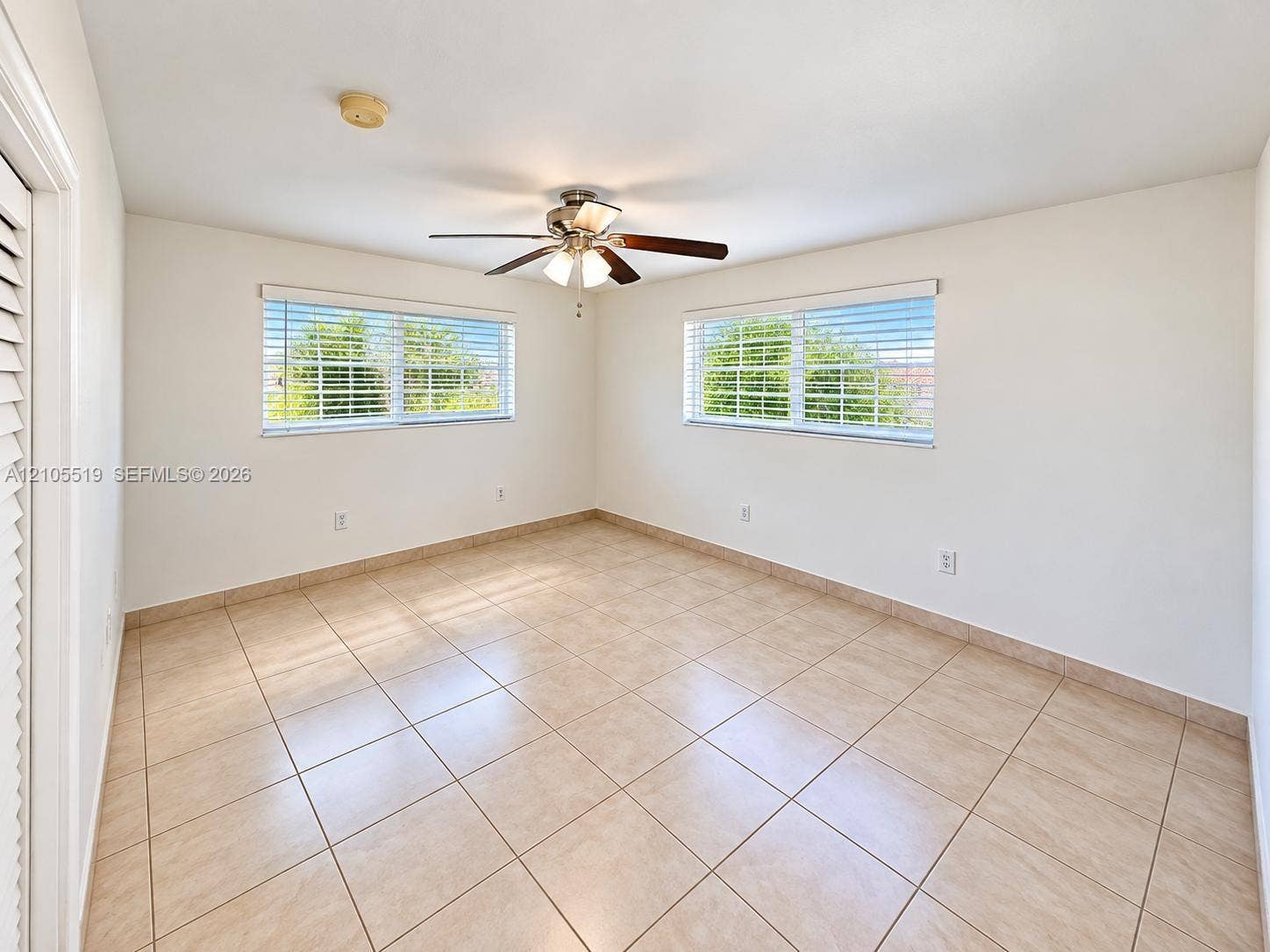 Neutral-toned tile flooring, two windows with horizontal blinds, and a ceiling fan with light fixture