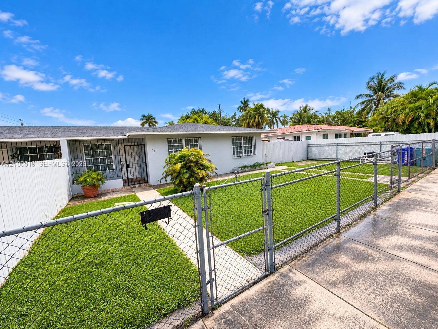 White stucco exterior with a gray shingle roof, chain-link fencing, and a white picket fence enclosing the property