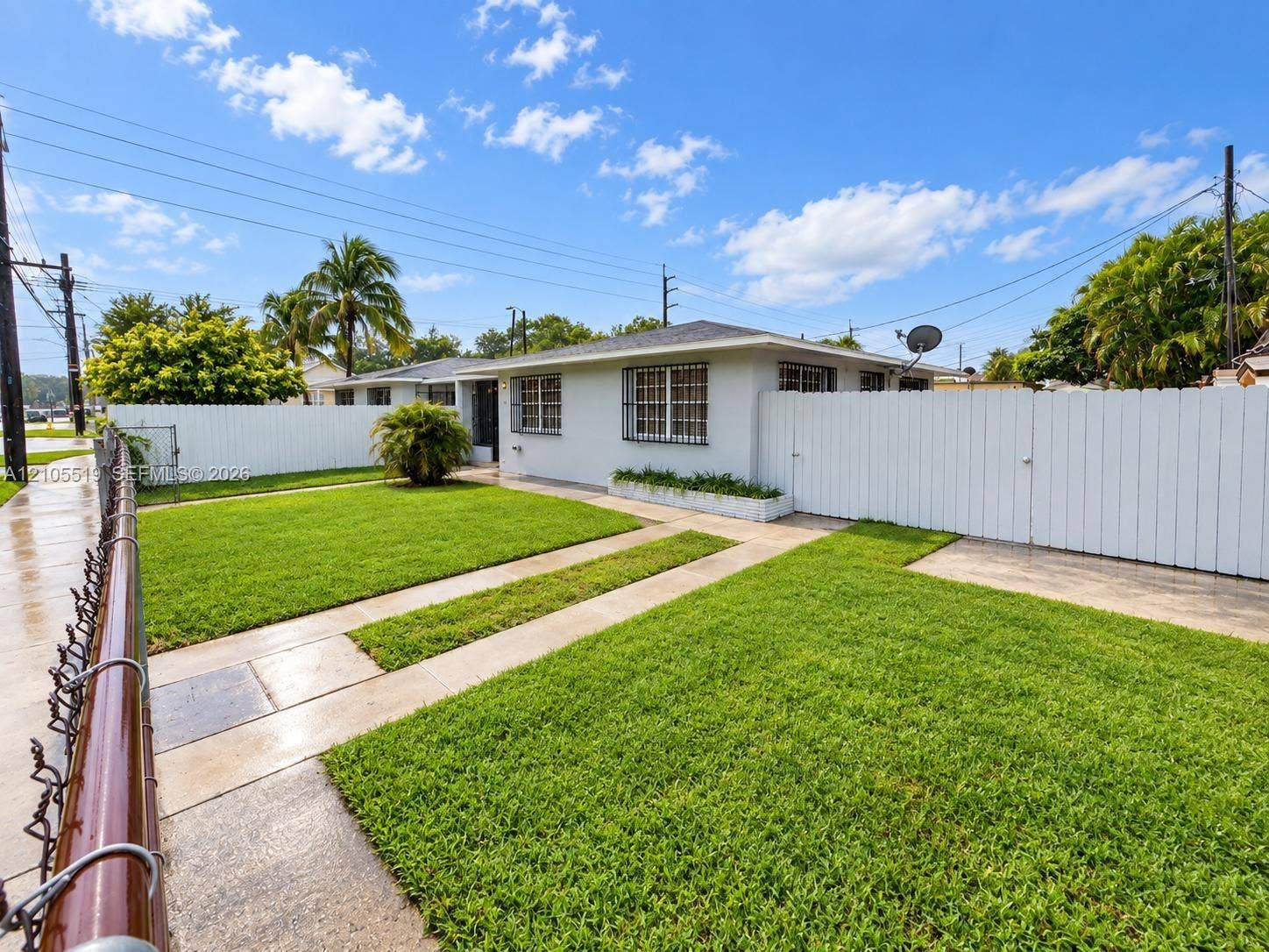 Fenced front yard featuring a manicured lawn, concrete walkway, and white privacy fence