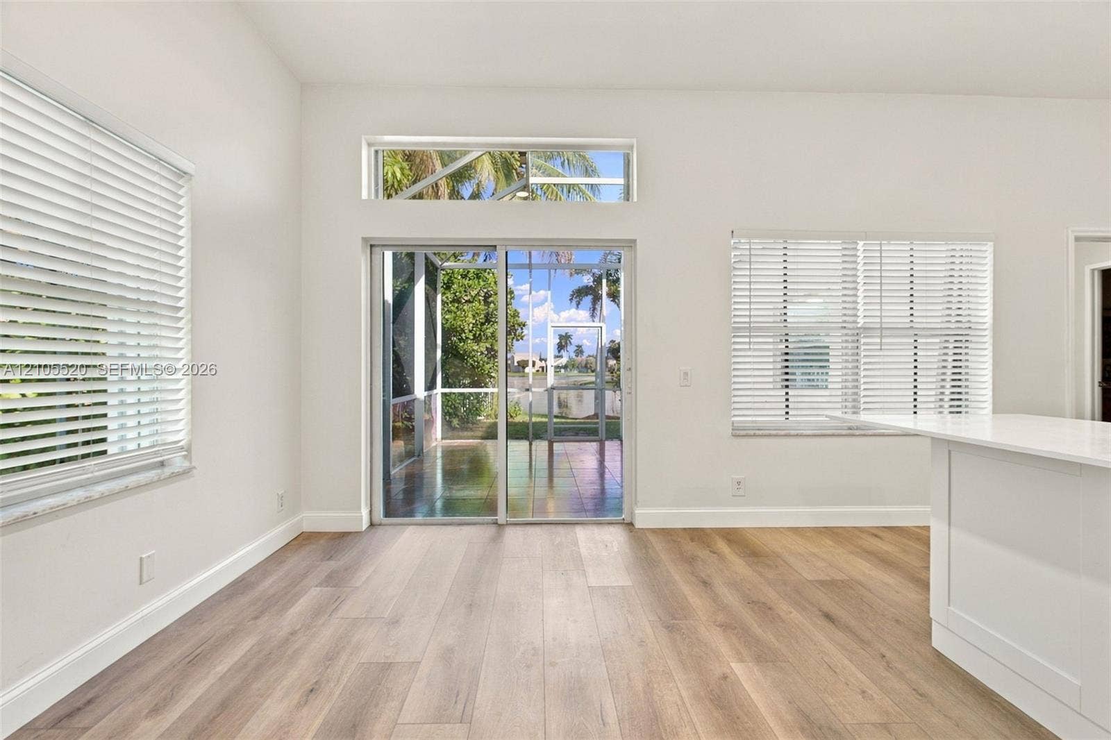 649 Willow Bend Road, Weston, Weston, FL 33327 Interior space featuring wood-finish flooring, white walls, horizontal window blinds, sliding glass patio door with a transom window, and a built-in white kitchen peninsula