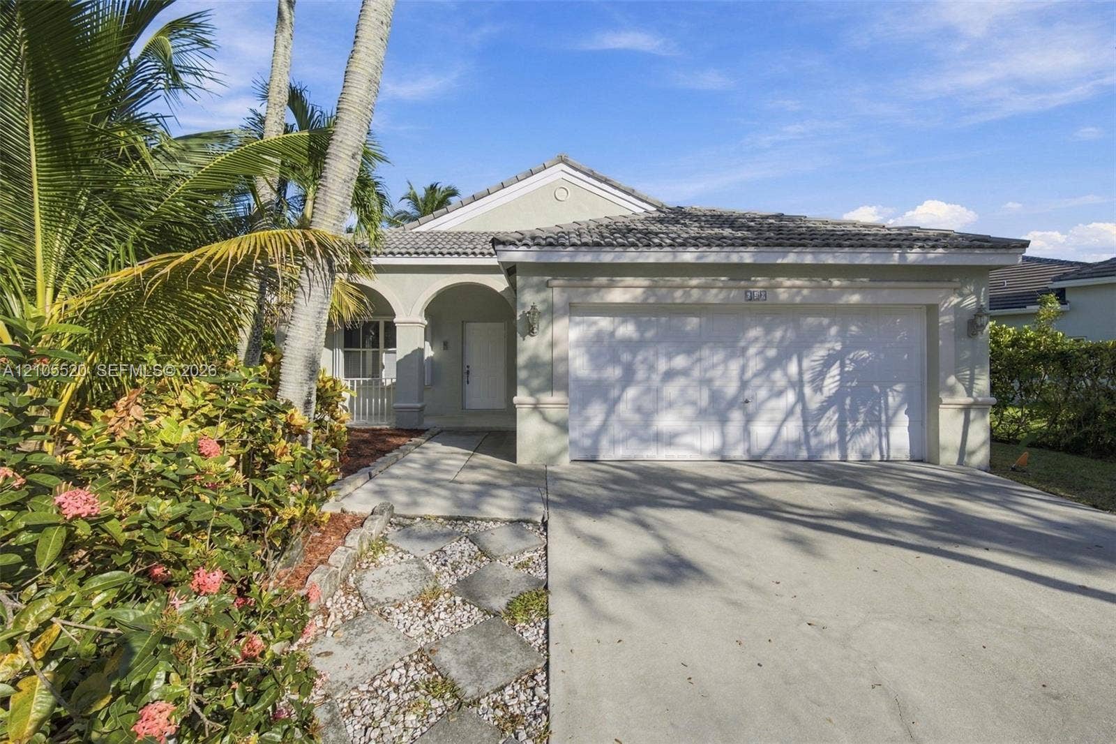 649 Willow Bend Road, Weston, Weston, FL 33327 Single-story exterior featuring a concrete tile roof, arched entryway, and two-car garage, complemented by a stone paver walkway and established tropical landscaping
