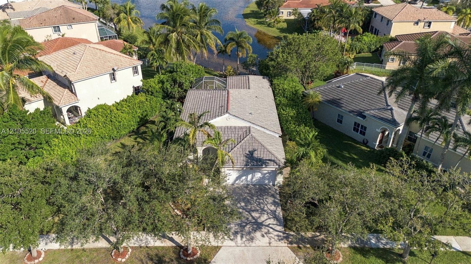 649 Willow Bend Road, Weston, Weston, FL 33327 Aerial perspective featuring a concrete tile roof, paved driveway, enclosed rear patio, and mature landscaping on a waterfront lot