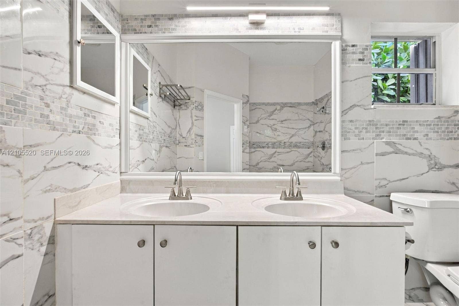 649 Willow Bend Road, Weston, Weston, FL 33327 Double vanity featuring a stone countertop, dual undermount sinks, large rectangular mirror, and full-height stone-finish wall tile with accent inlay
