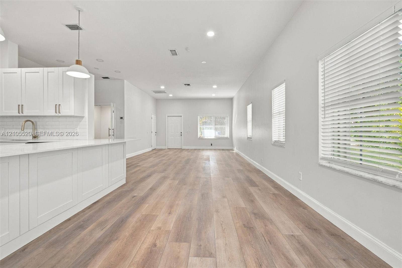 649 Willow Bend Road, Weston, Weston, FL 33327 Open-concept interior featuring wood-finish flooring, white shaker-style cabinetry, a quartz-topped island, recessed lighting, and horizontal window blinds