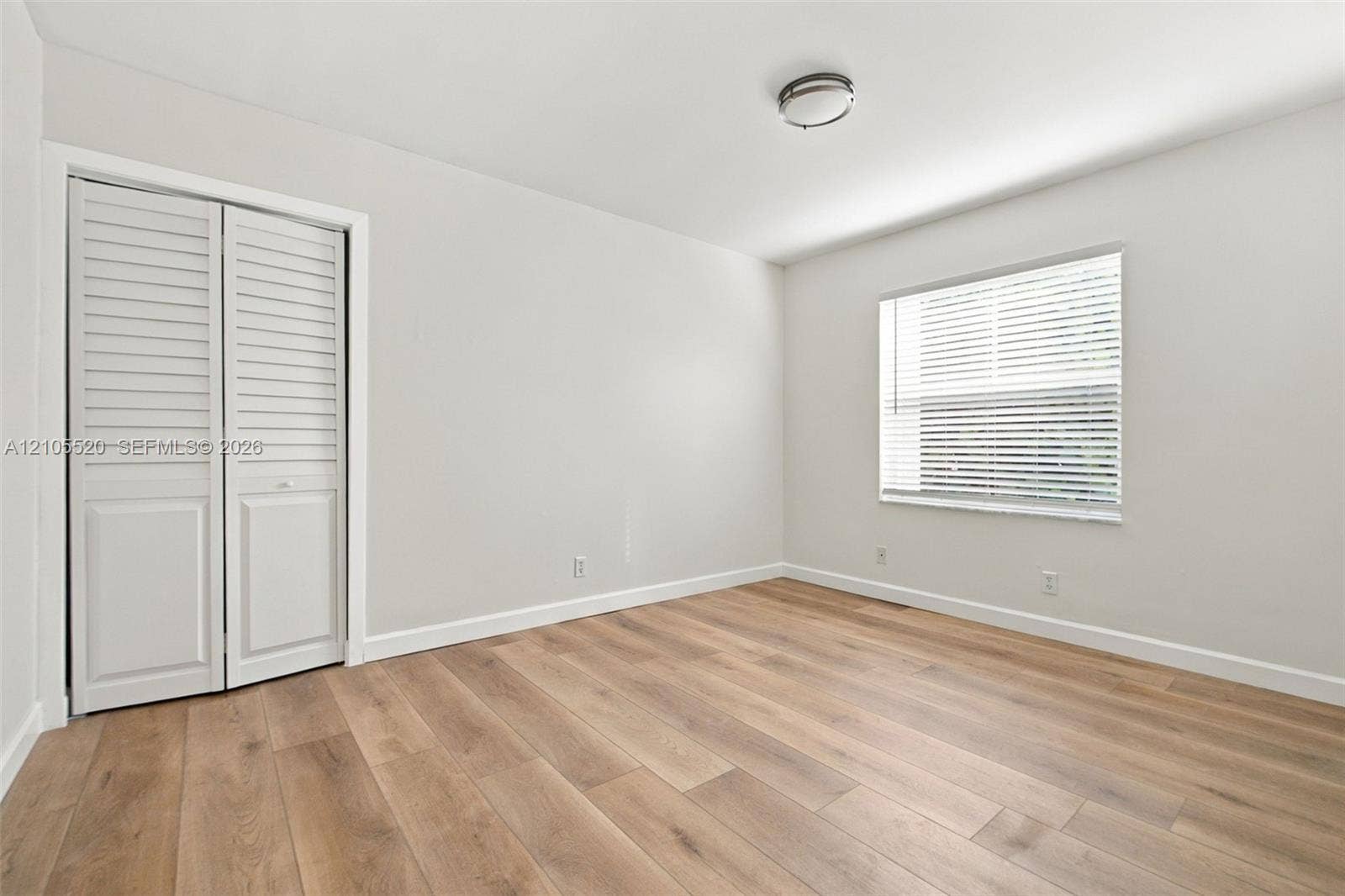649 Willow Bend Road, Weston, Weston, FL 33327 Interior room featuring wood-finish flooring, neutral wall paint, a double-panel louvered closet door, a single-window configuration with horizontal blinds, and a flush-mount ceiling light fixture