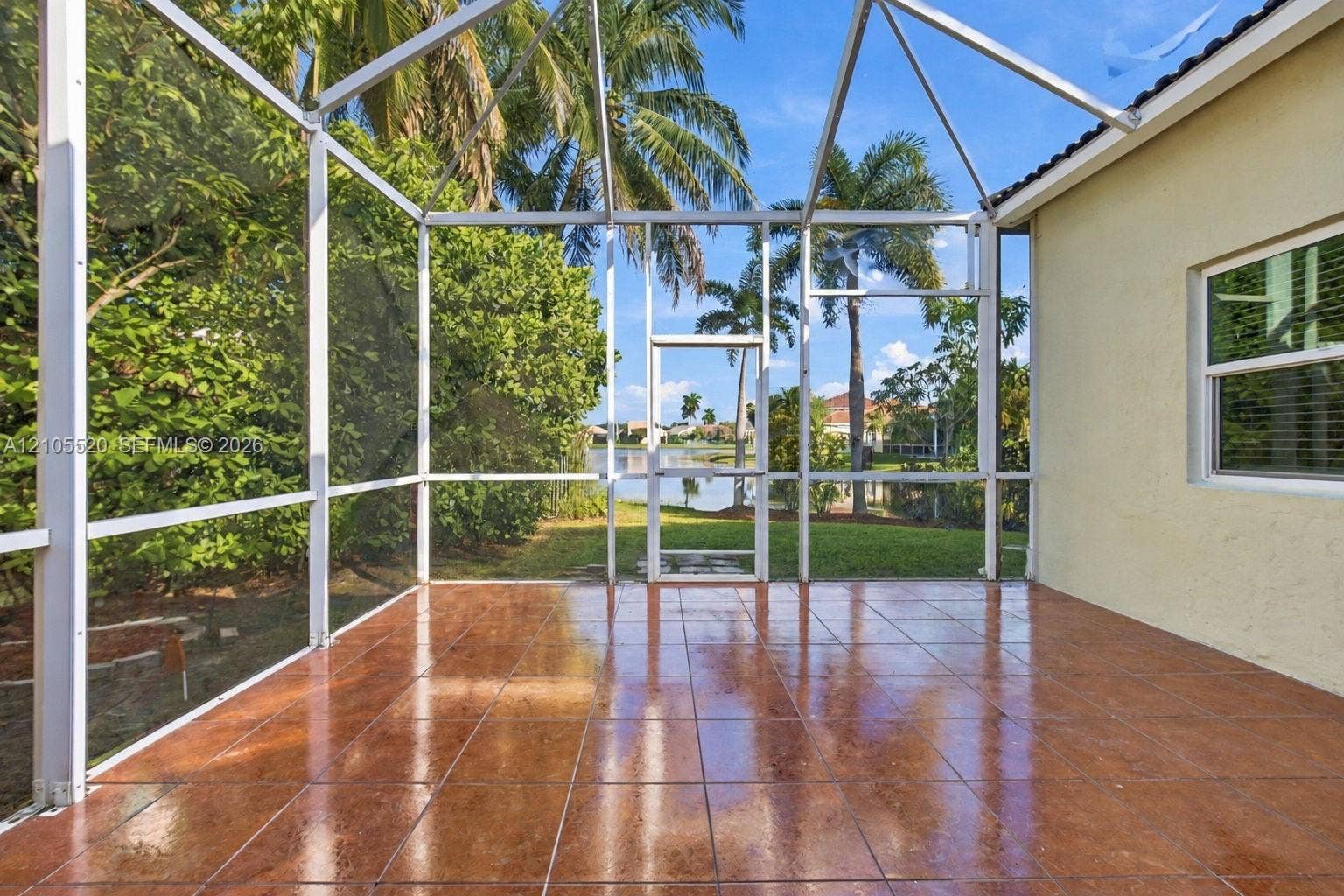 649 Willow Bend Road, Weston, Weston, FL 33327 Screened lanai featuring tile flooring, a metal frame enclosure, and a backdrop of mature palm trees and water