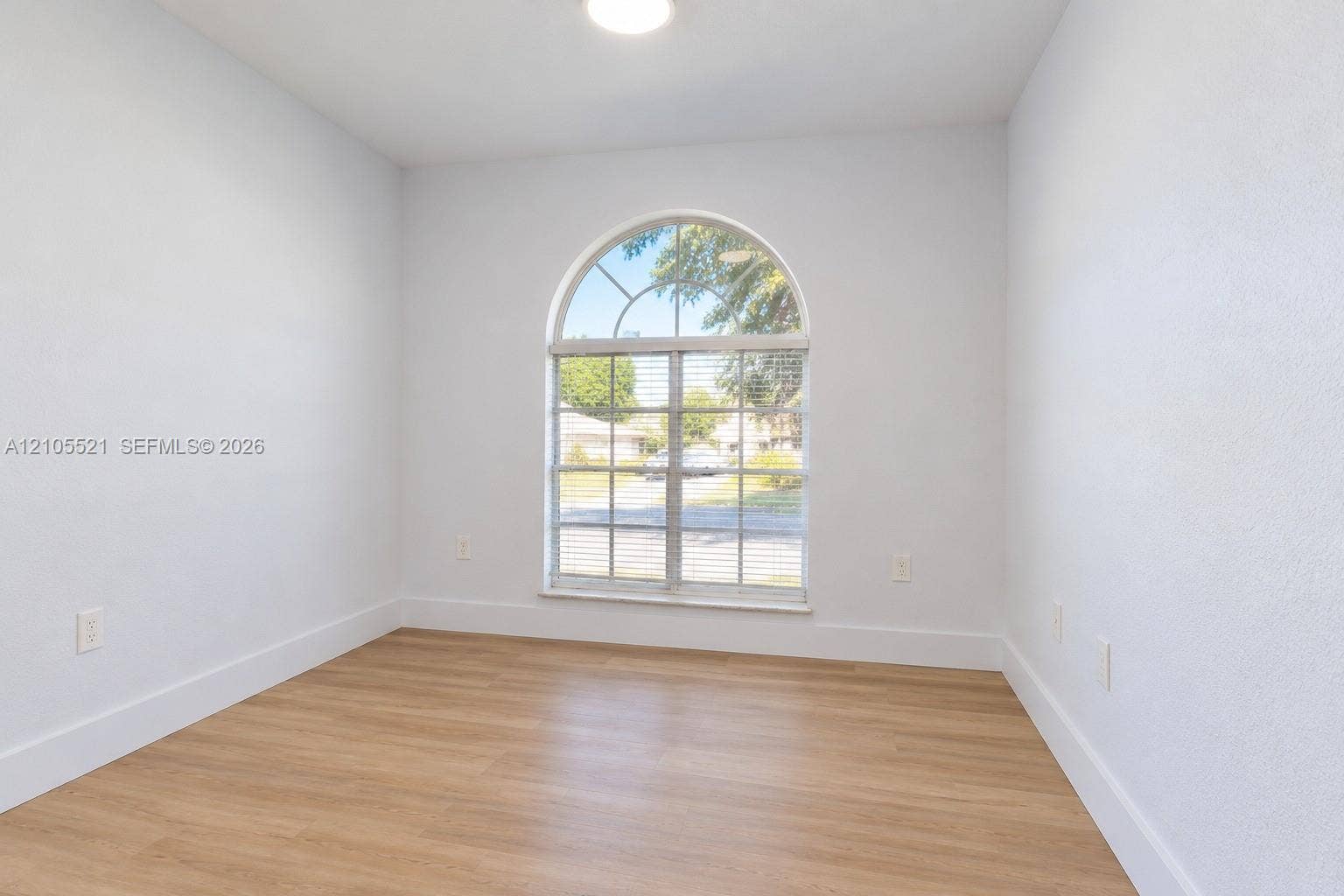 Arched window with blinds, wood-finish flooring, white walls, and a ceiling light fixture