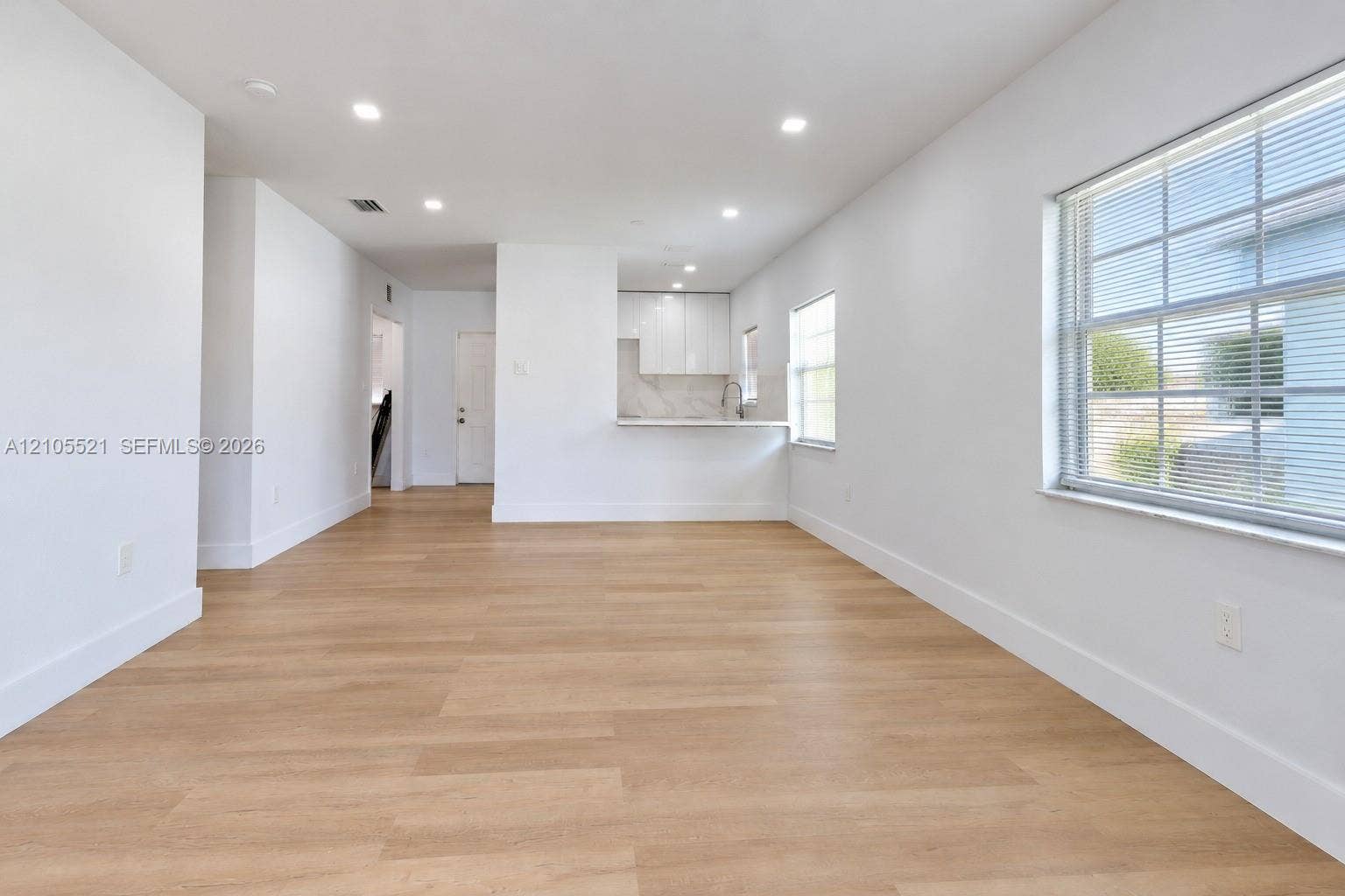 Open-concept living area featuring wood-finish flooring, recessed lighting, white walls, and a kitchen pass-through with a breakfast bar