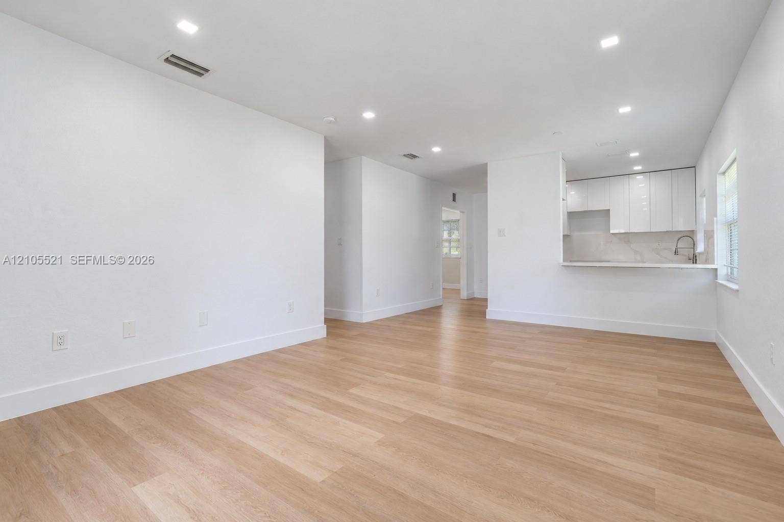 Recessed lighting illuminates the open-concept living space, featuring wood-finish flooring and a breakfast bar with a solid surface countertop