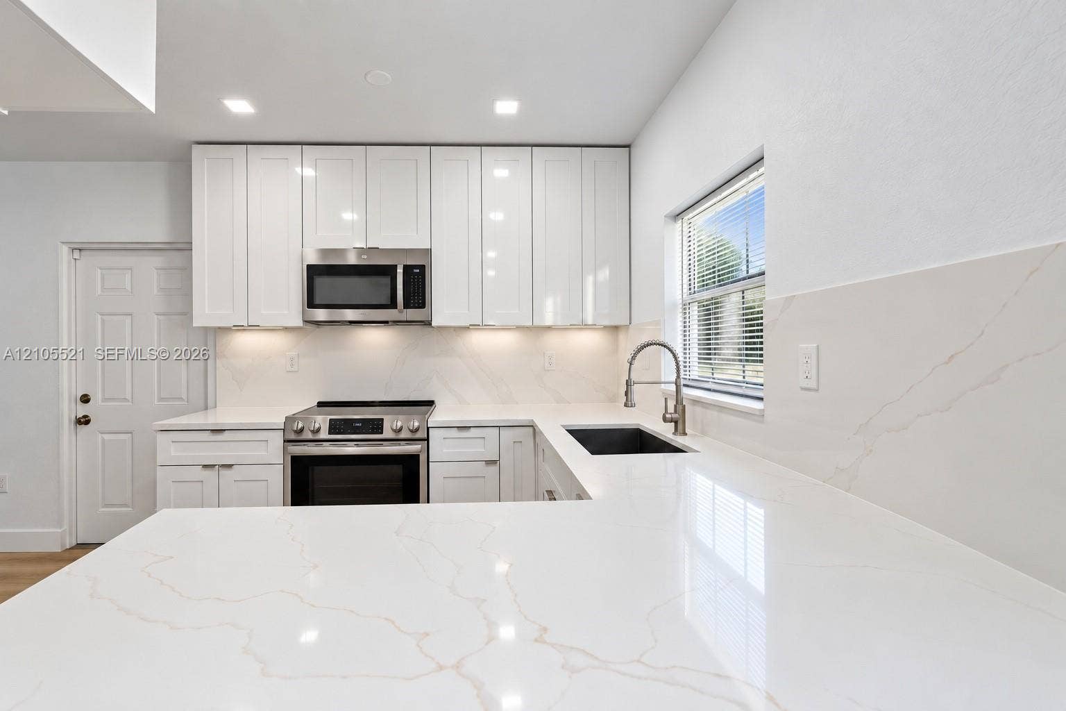 White shaker-style cabinetry with under-cabinet lighting, stainless steel appliances, and a stainless steel sink with a gooseneck faucet
