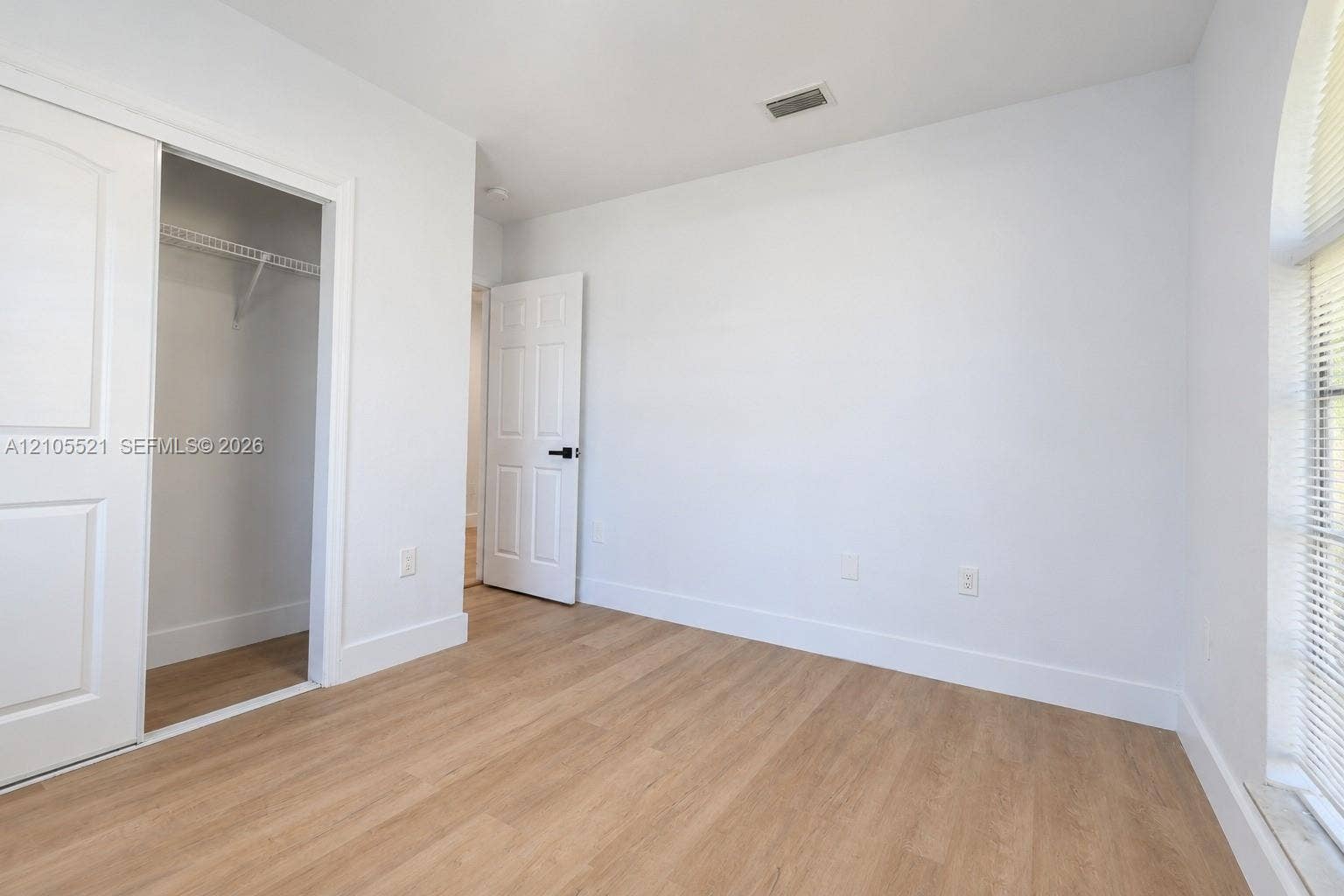 Wood-finish flooring, white walls, white trim, sliding closet doors, and a window with blinds