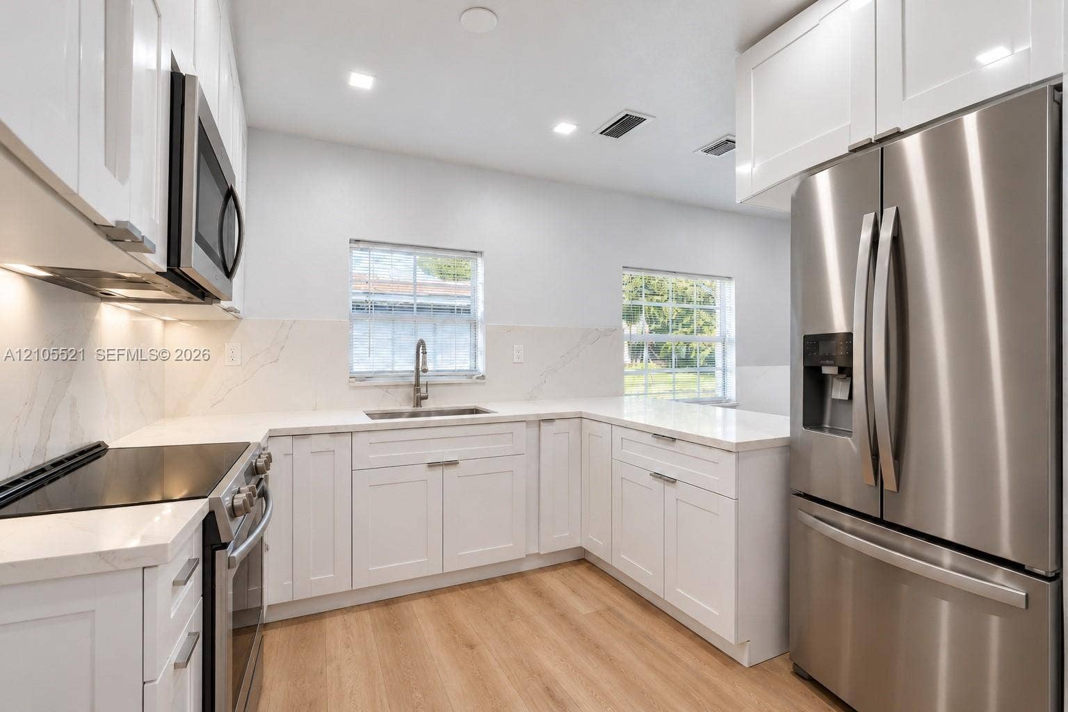 Updated kitchen featuring white shaker cabinetry, stainless steel appliances, light-toned wood-finish flooring, and white countertops with a matching backsplash