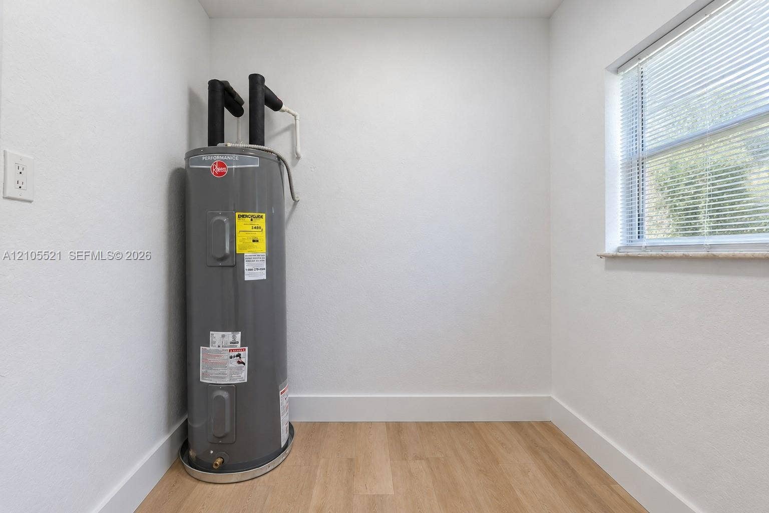 Water heater, wood-finish flooring, white walls, window with blinds, and white trim