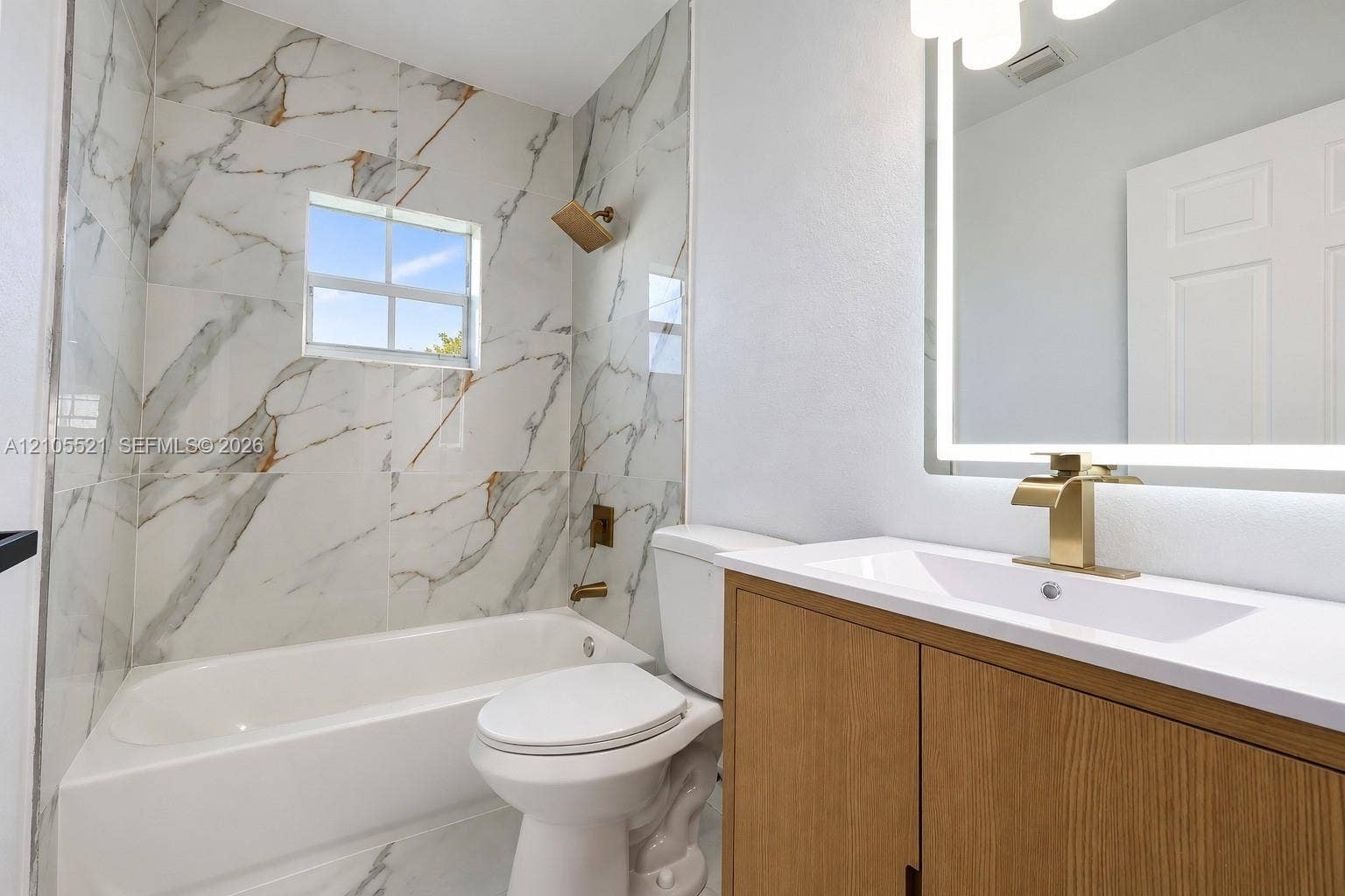Bathroom featuring a single vanity with wood-finish cabinetry, a white countertop, and a lighted mirror