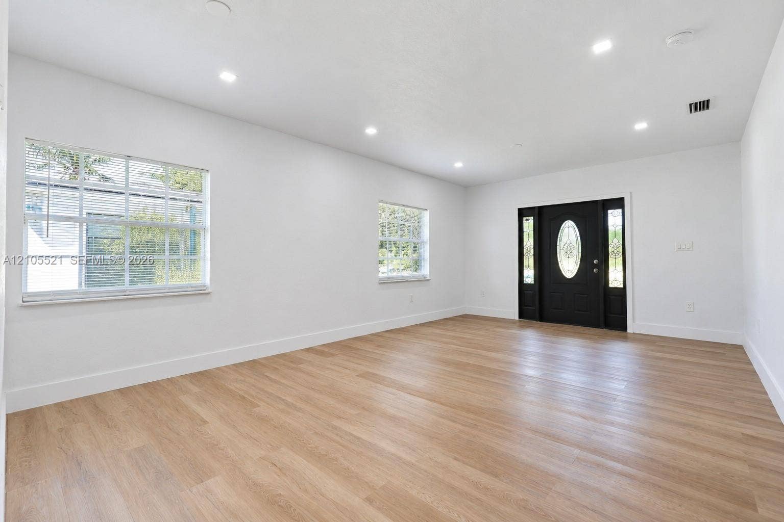 Spacious room featuring wood-finish flooring, recessed lighting, and a black front door with an oval glass insert and sidelights