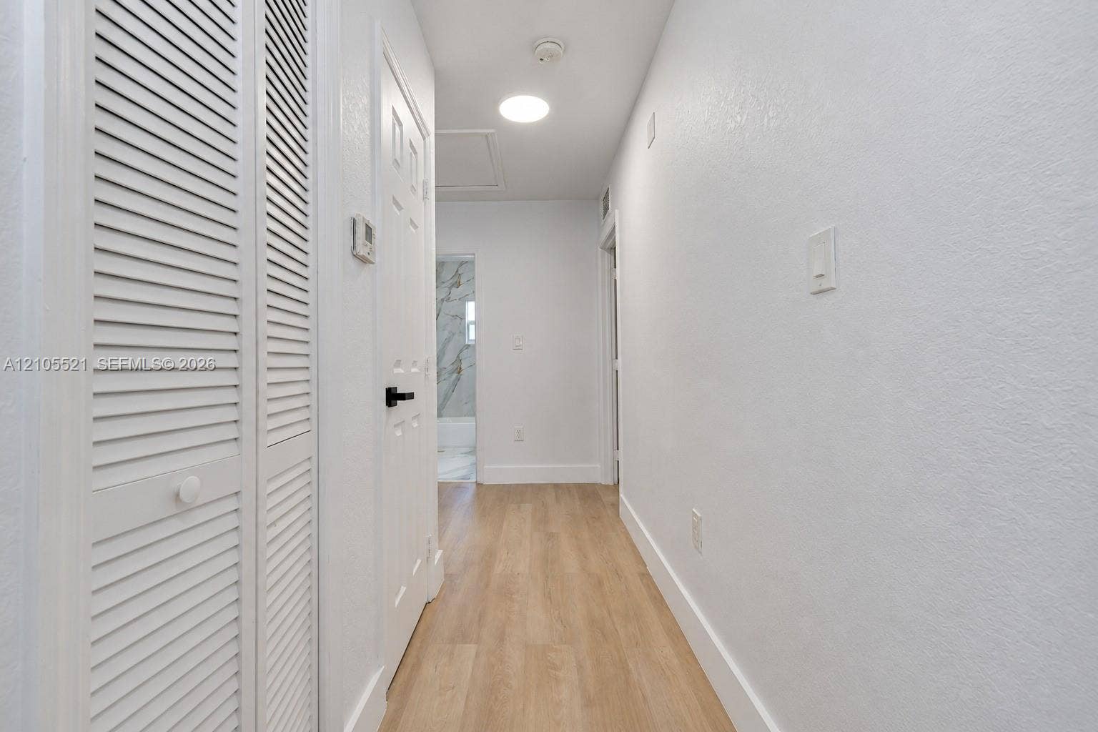 Hallway featuring wood-finish flooring, white walls, louvered closet doors, and recessed lighting
