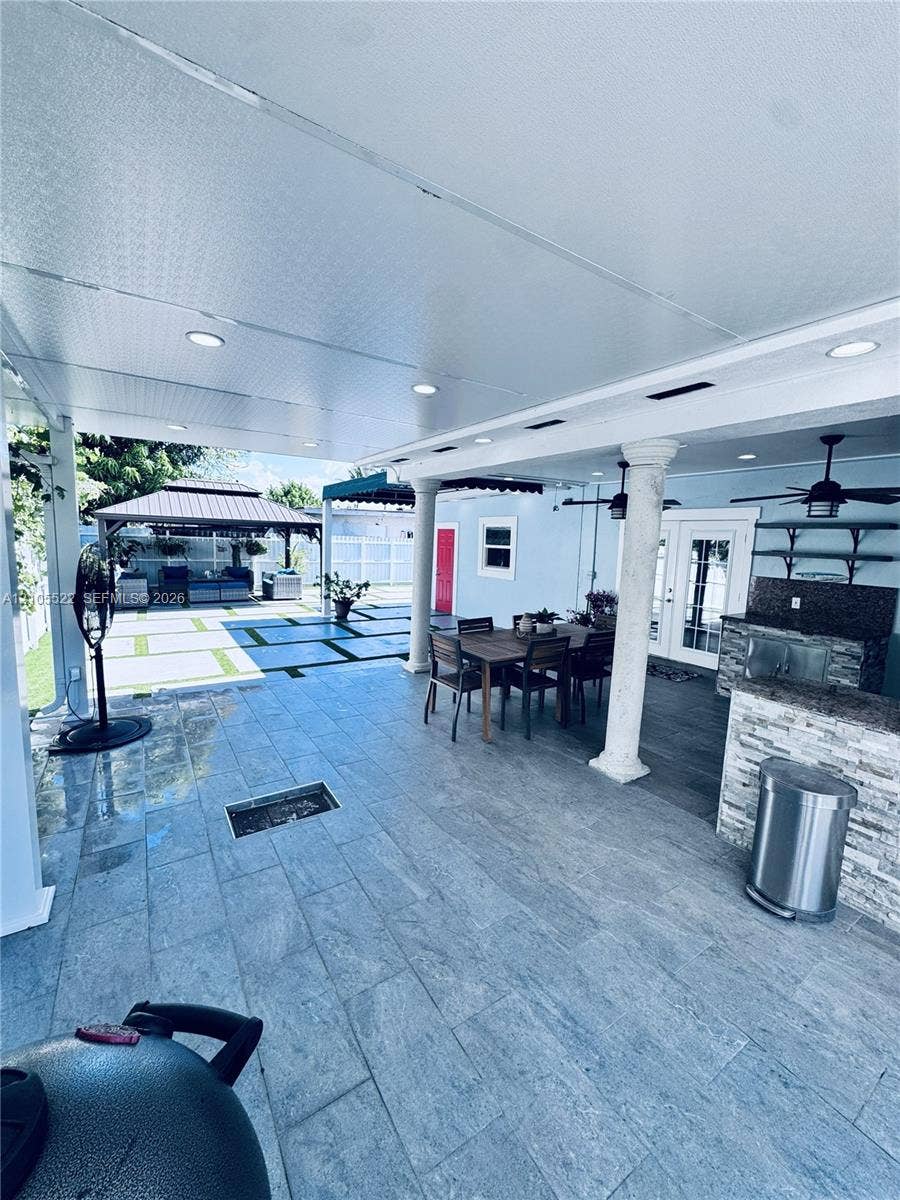 Covered patio with recessed lighting, stone tile flooring, an outdoor kitchen, and decorative columns
