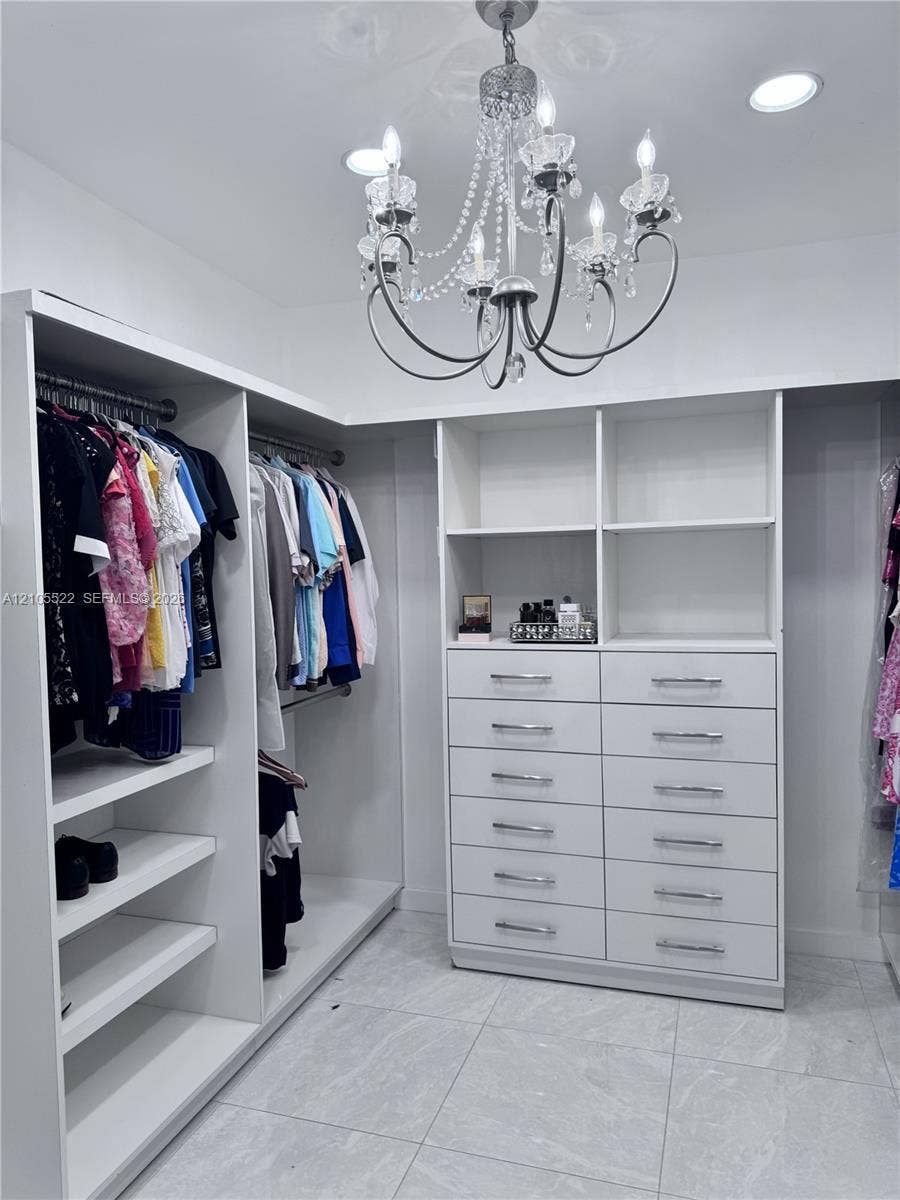 Built-in closet system featuring white shelving, multiple hanging rods, and an integrated dresser with chrome pulls
