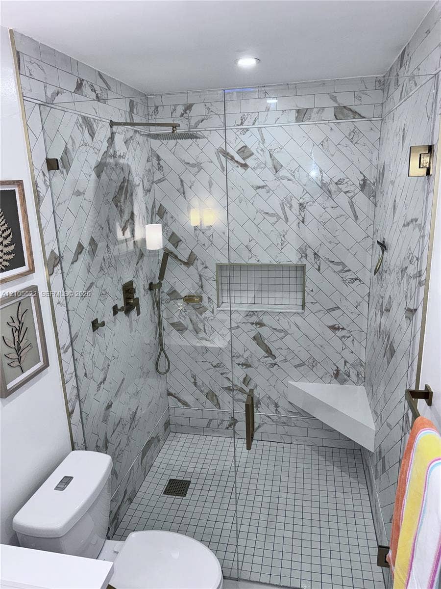 Glass-enclosed shower with herringbone pattern wall tile, a built-in corner bench, recessed niche, and square tile flooring