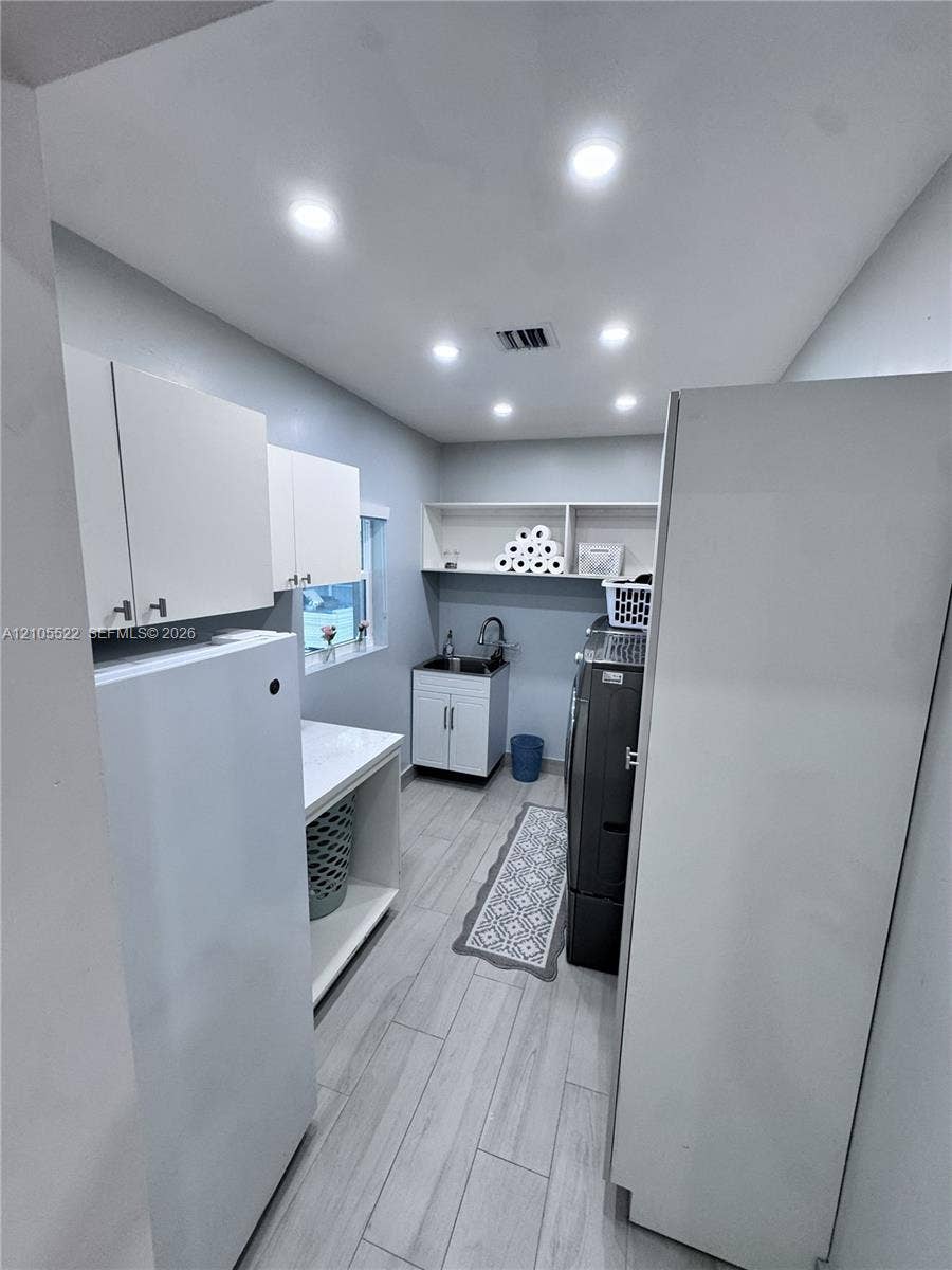 Recessed lighting, wood-finish flooring, built-in shelving, white cabinetry, and a utility sink