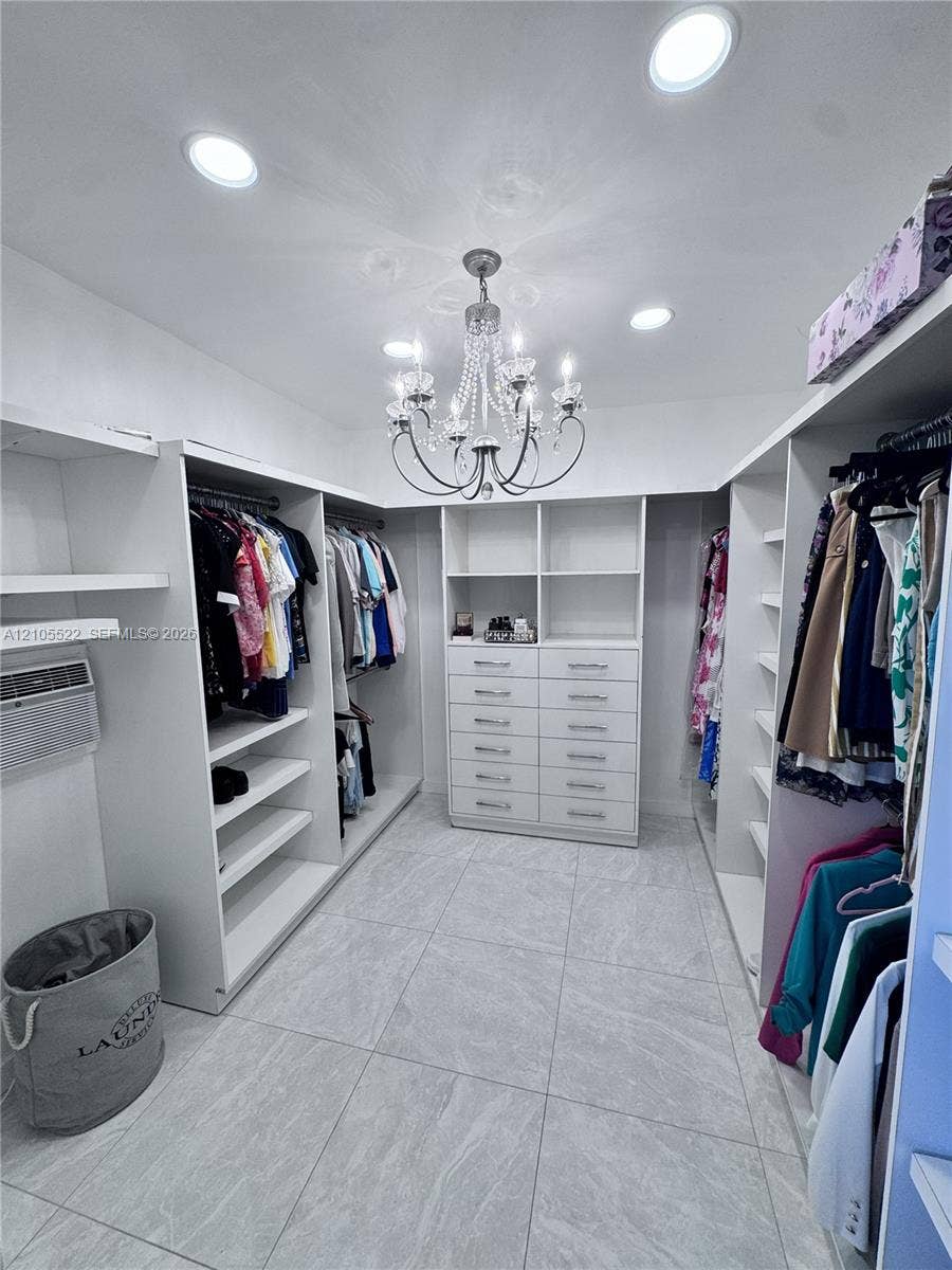 Walk-in closet featuring extensive built-in shelving, integrated drawers, recessed lighting, a central chandelier, and large format floor tiles