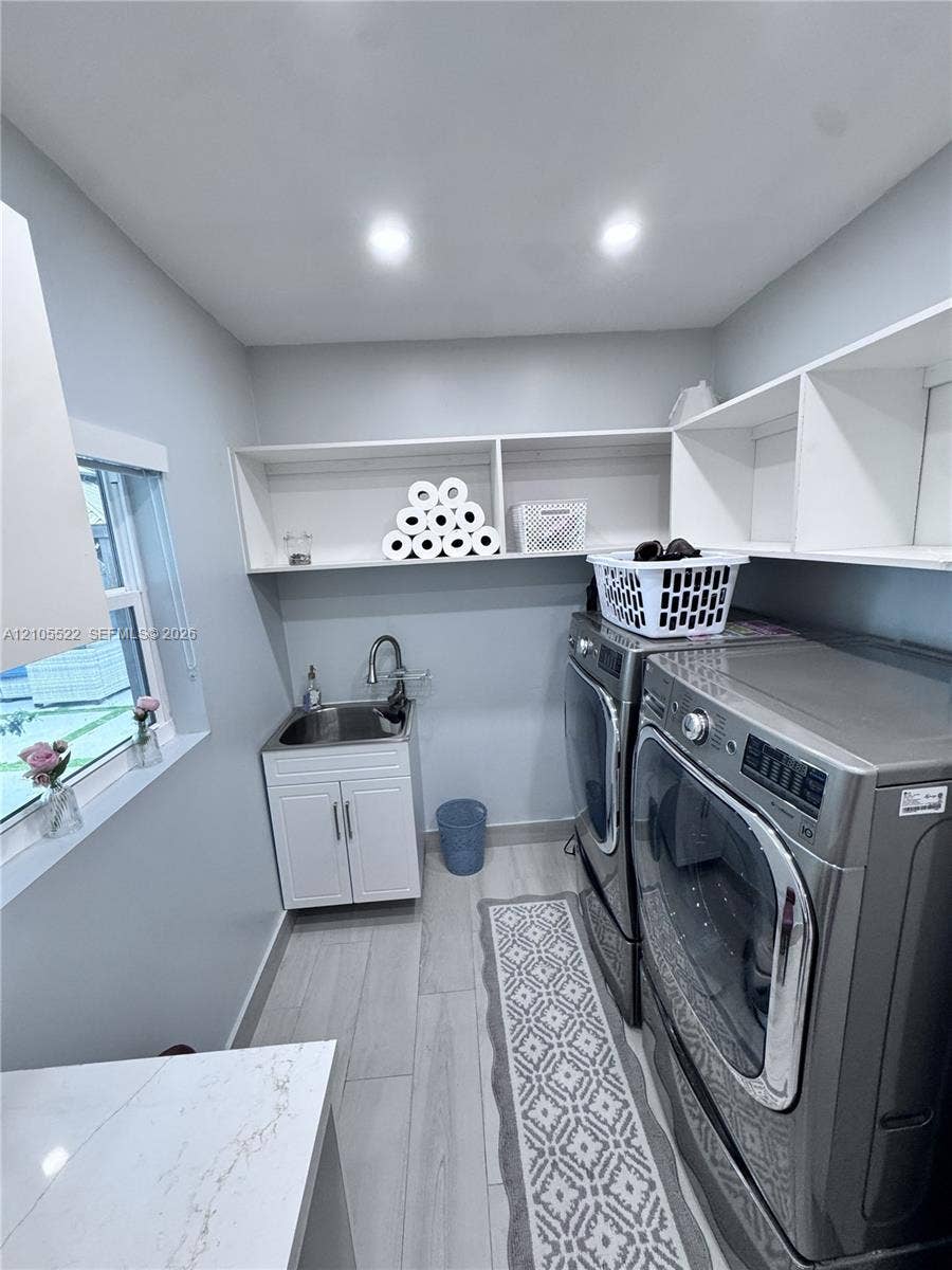 Laundry space featuring wood-finish flooring, built-in shelving, a utility sink with cabinetry, and a window