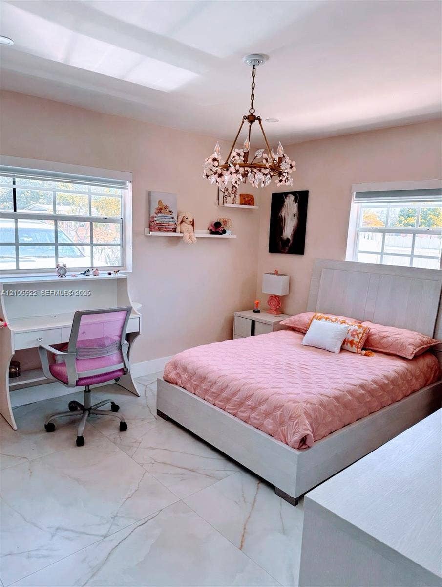 Recessed lighting, ornate chandelier, large windows with white trim, white desk with integrated shelving, and white tile flooring