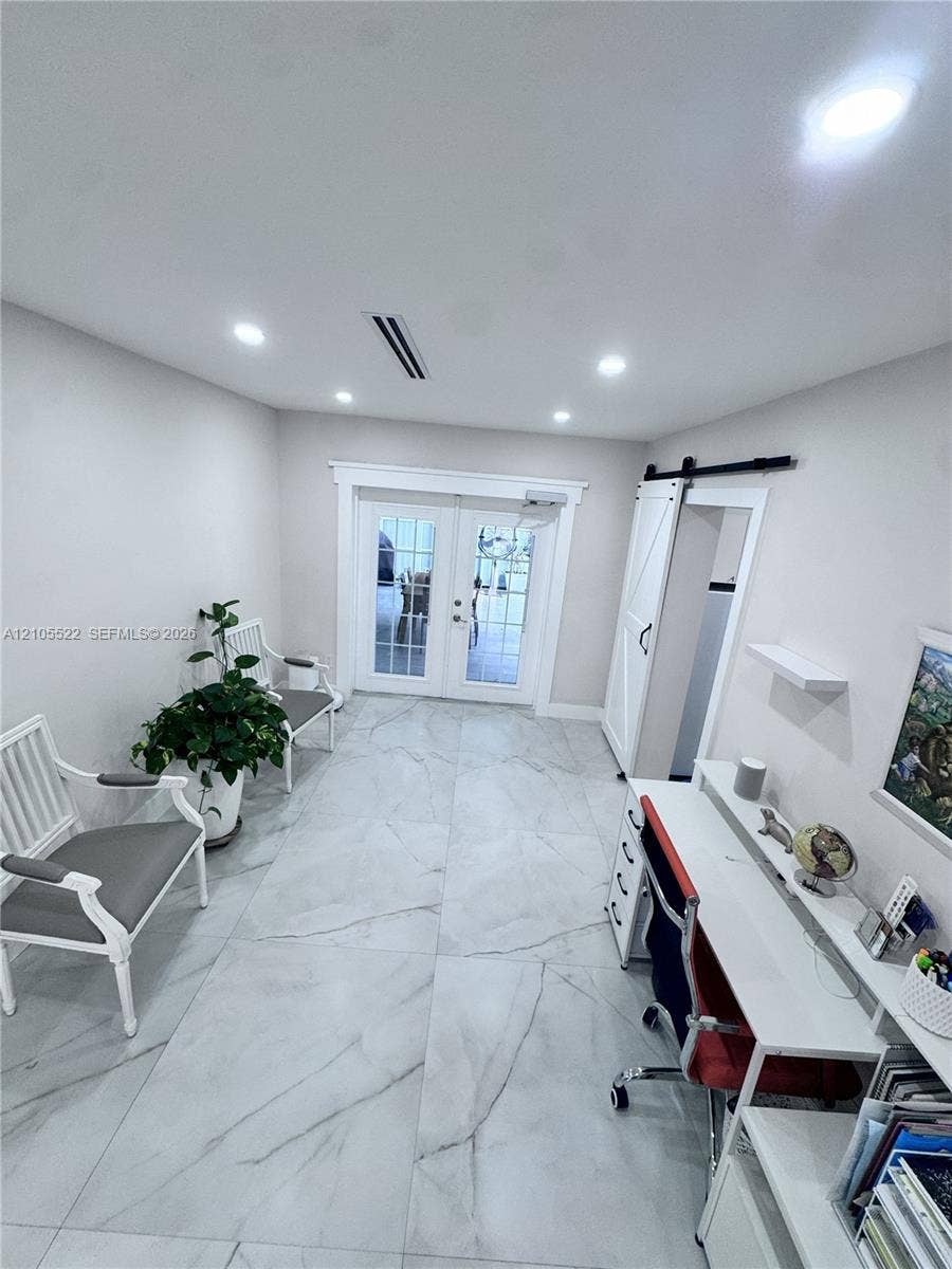 Recessed lighting illuminates the space, featuring large format tile flooring and white french doors