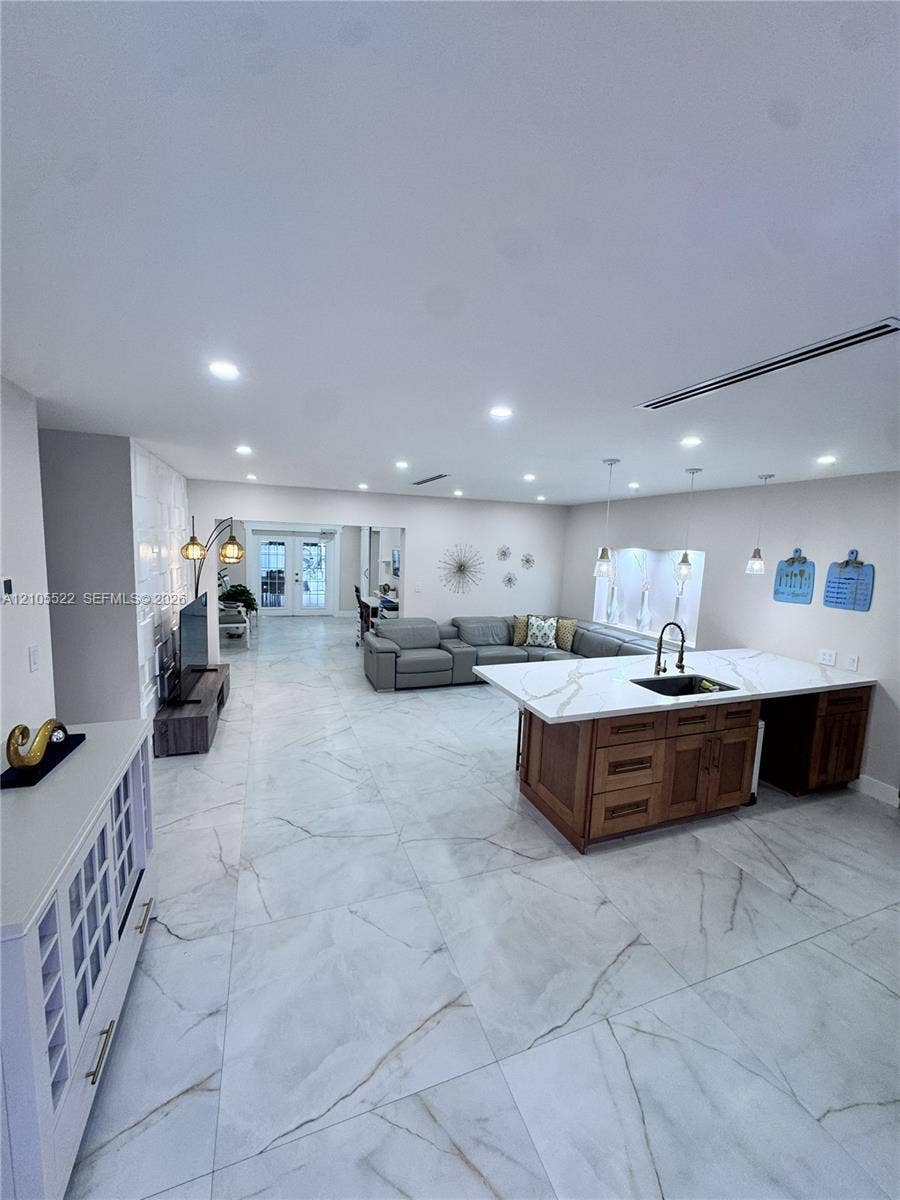 Open-concept living space with large format tile flooring, recessed lighting, and a kitchen island featuring a black sink and faucet