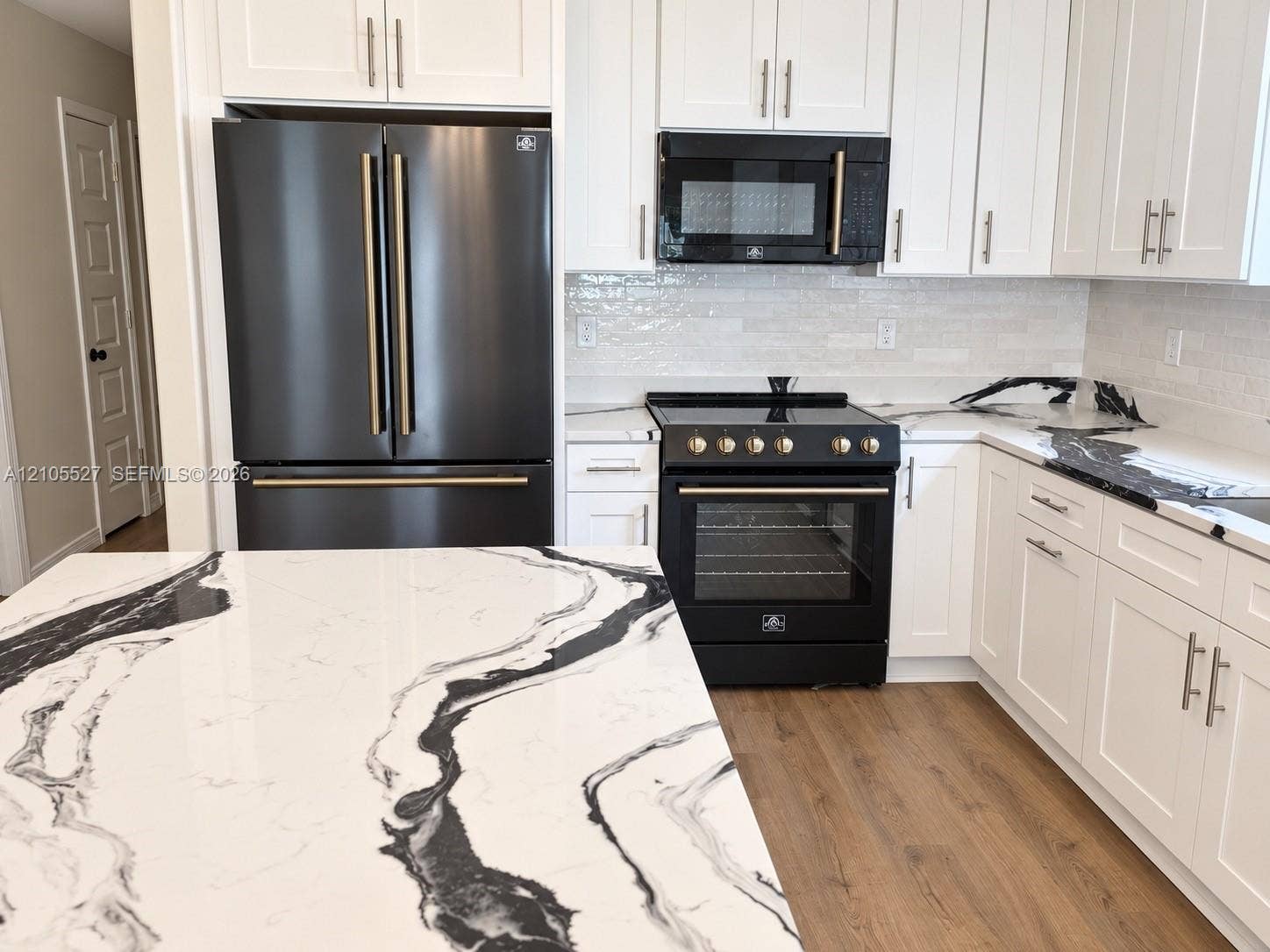 White shaker cabinetry with matte black appliances, wood-finish flooring, and a patterned countertop