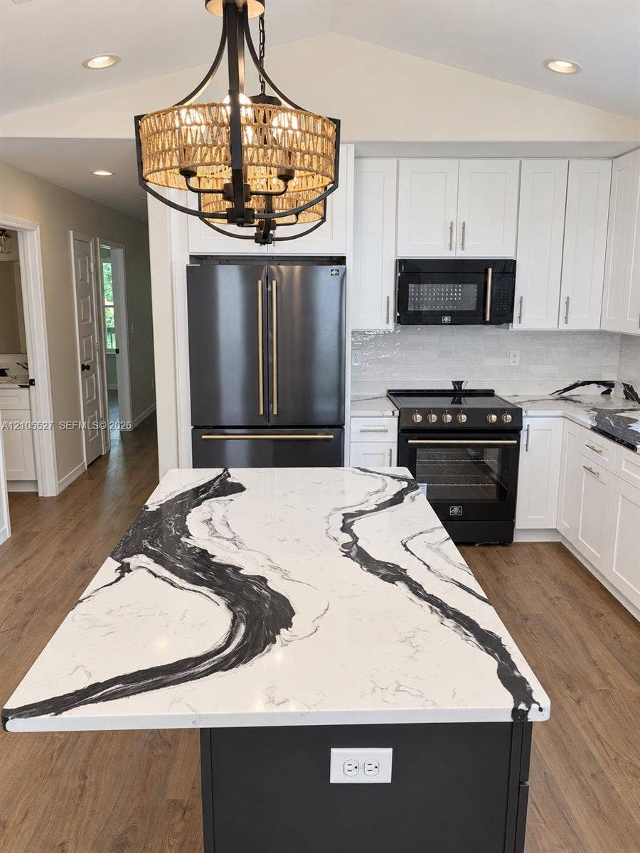 Kitchen featuring white upper cabinetry, dark lower island cabinetry, dark stainless steel appliances, wood-finish flooring, and a decorative chandelier