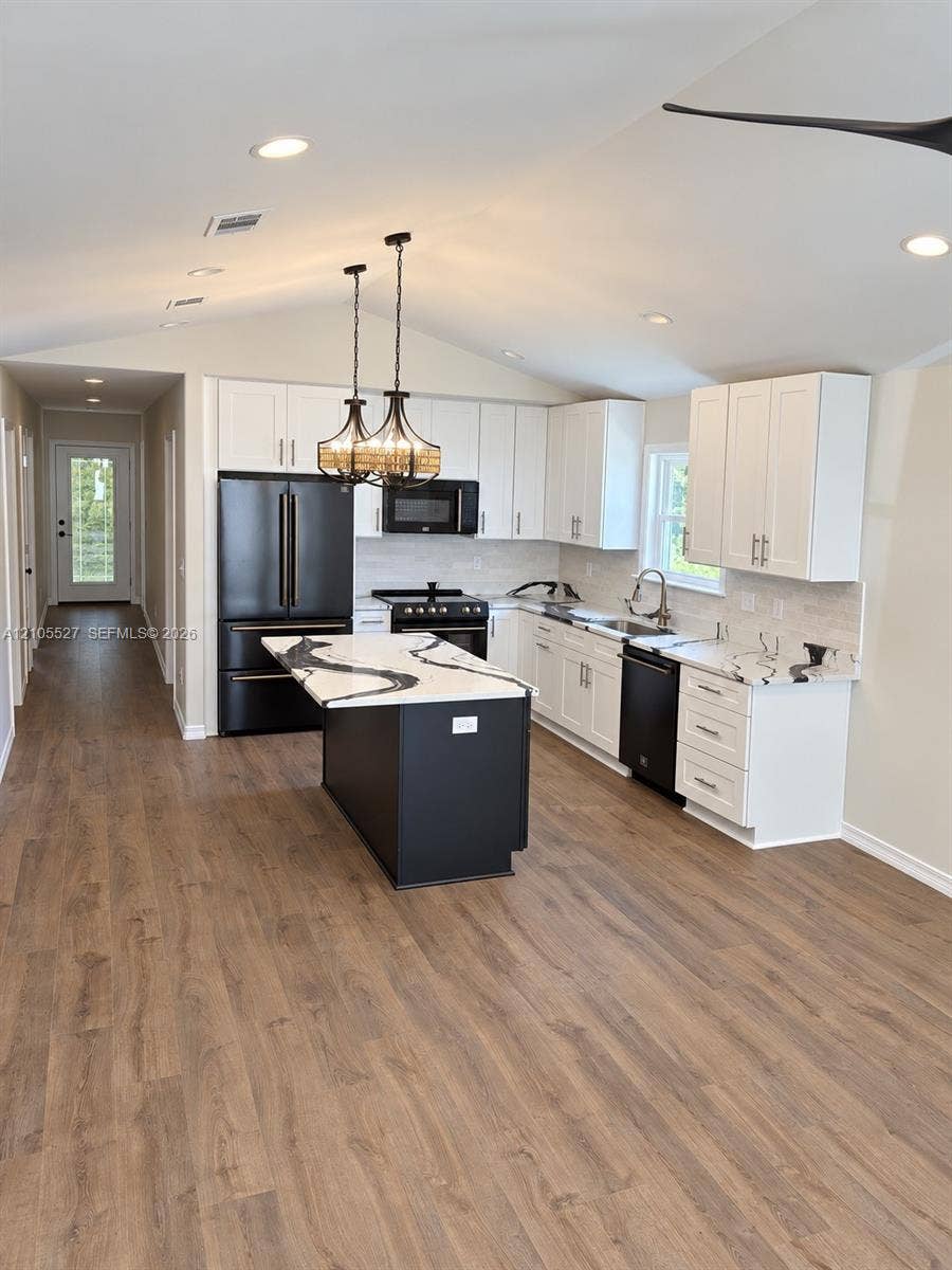 Vaulted ceiling with recessed lighting, wood-finish flooring, white cabinetry, a black kitchen island with a light-toned countertop, and black appliances