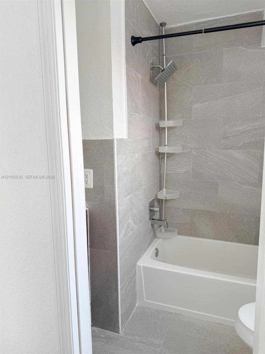 Bathtub and shower combination with light gray tiled surround and coordinating floor tiles