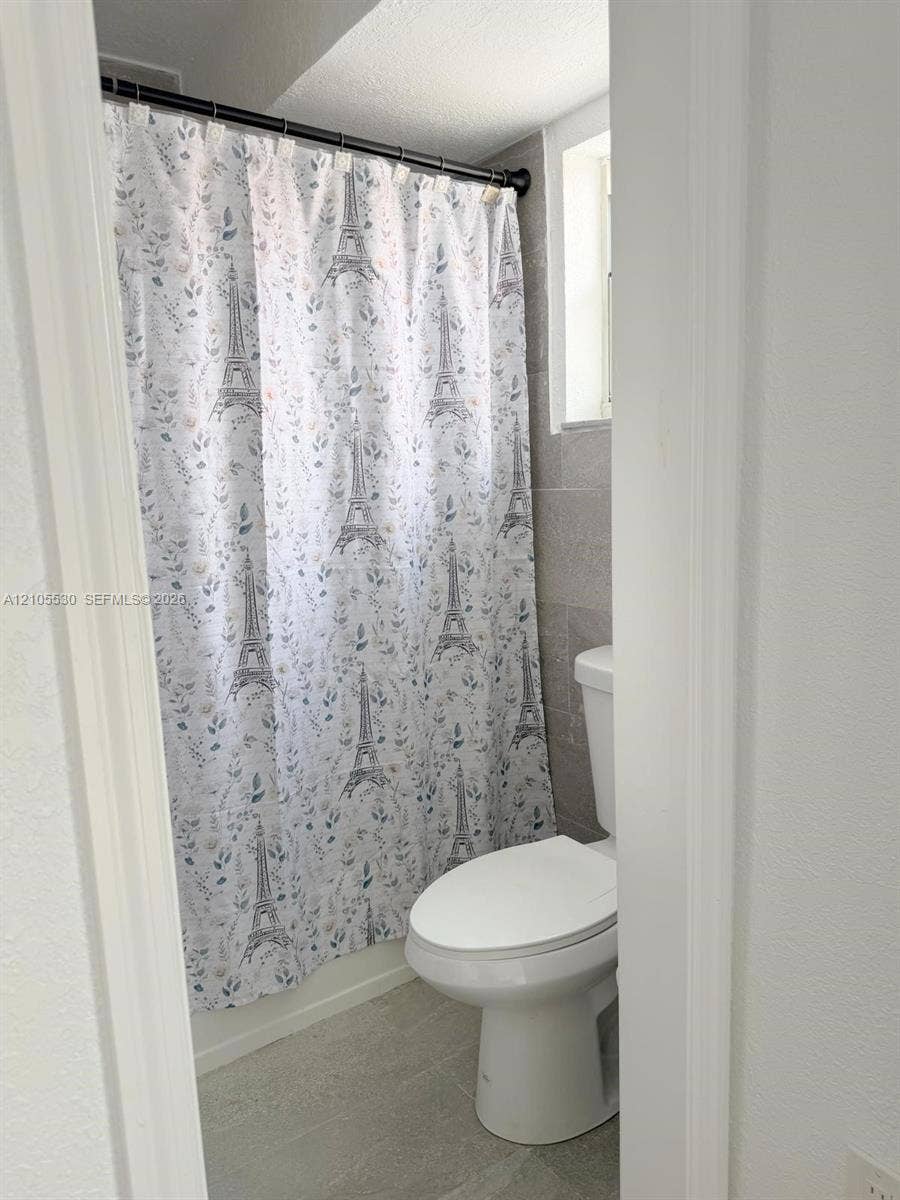 Tiled shower surround with a white toilet and light-toned flooring