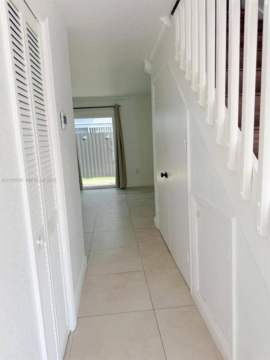 Tile flooring, white louvered bifold doors, white interior doors, white staircase balusters, and a sliding glass door